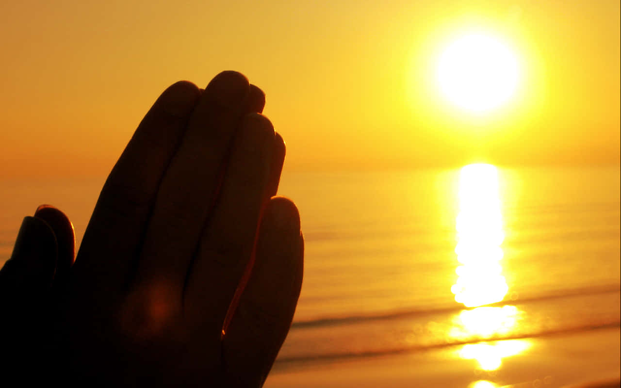 hands 桌布 壁紙 — 剪影雙手合十祈禱，映襯著金色夕陽在平靜海面上的倒影。