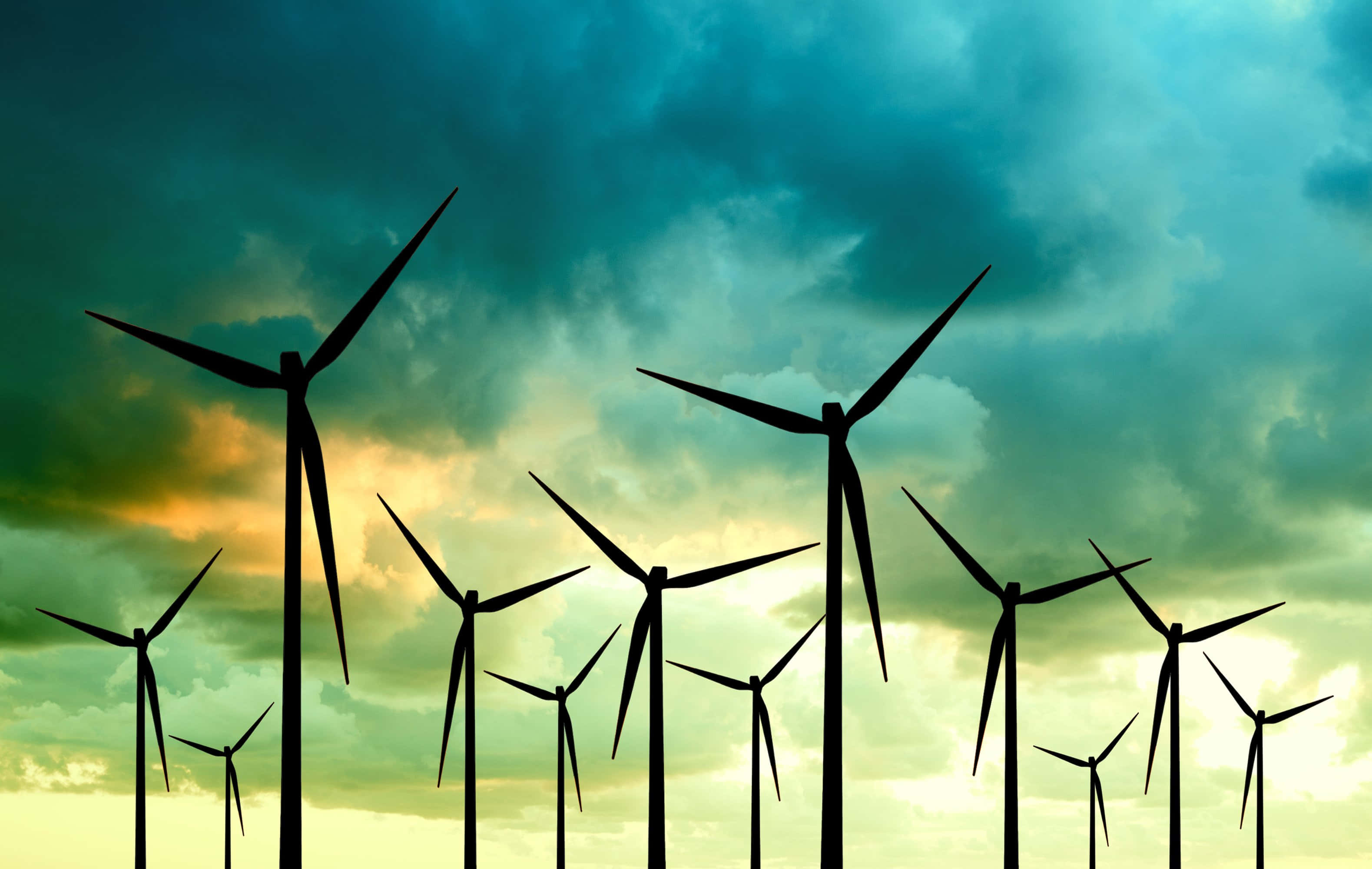 Energy 桌布 壁紙 — 剪影風力渦輪機在戲劇性的青綠色和金色日落天空與旋轉雲層中高聳矗立。