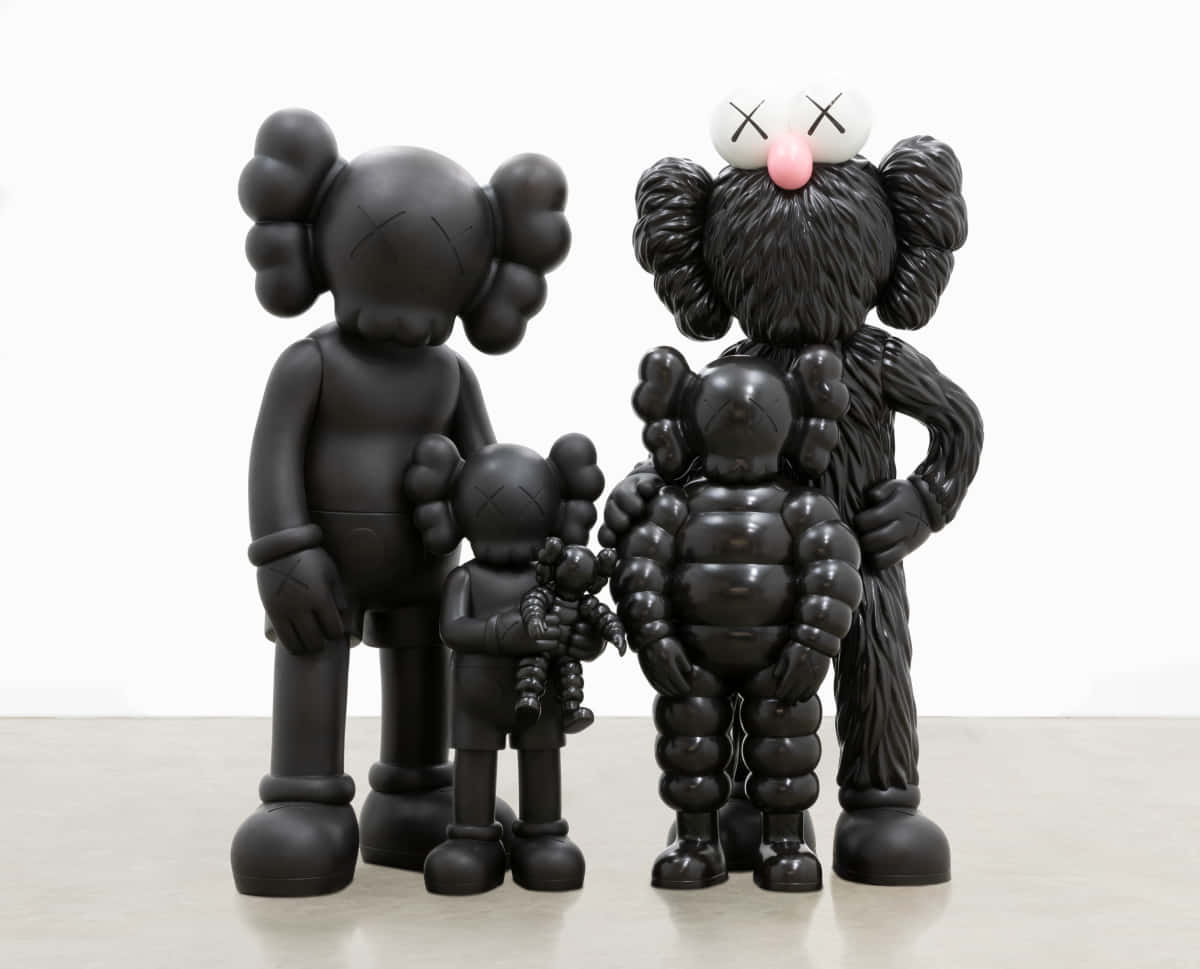 創意畫家 KAWS 壁紙 — 三件光澤黑色KAWS雕塑，帶有交叉的眼窩，一起站在淺色地板上，背景是白色牆壁。