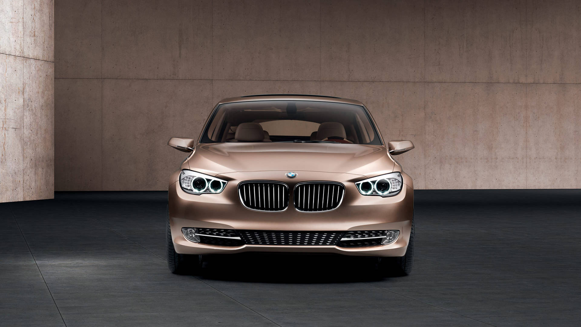 創新與優雅的完美結合：BMW混合動力車 壁紙 — 一輛時尚的青銅色寶馬轎車在簡約混凝土工作室中正面朝前，帶有戲劇性燈光。
