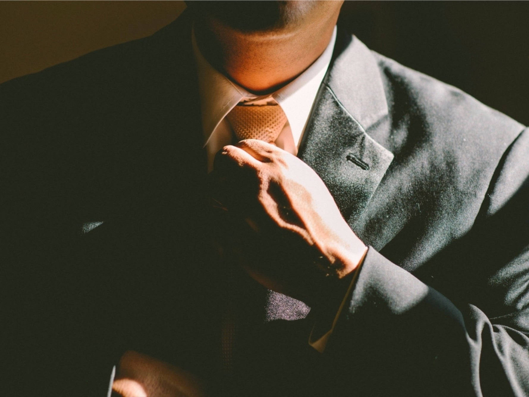 特寫一名男子在溫暖燈光下調整深色西裝中的領帶。