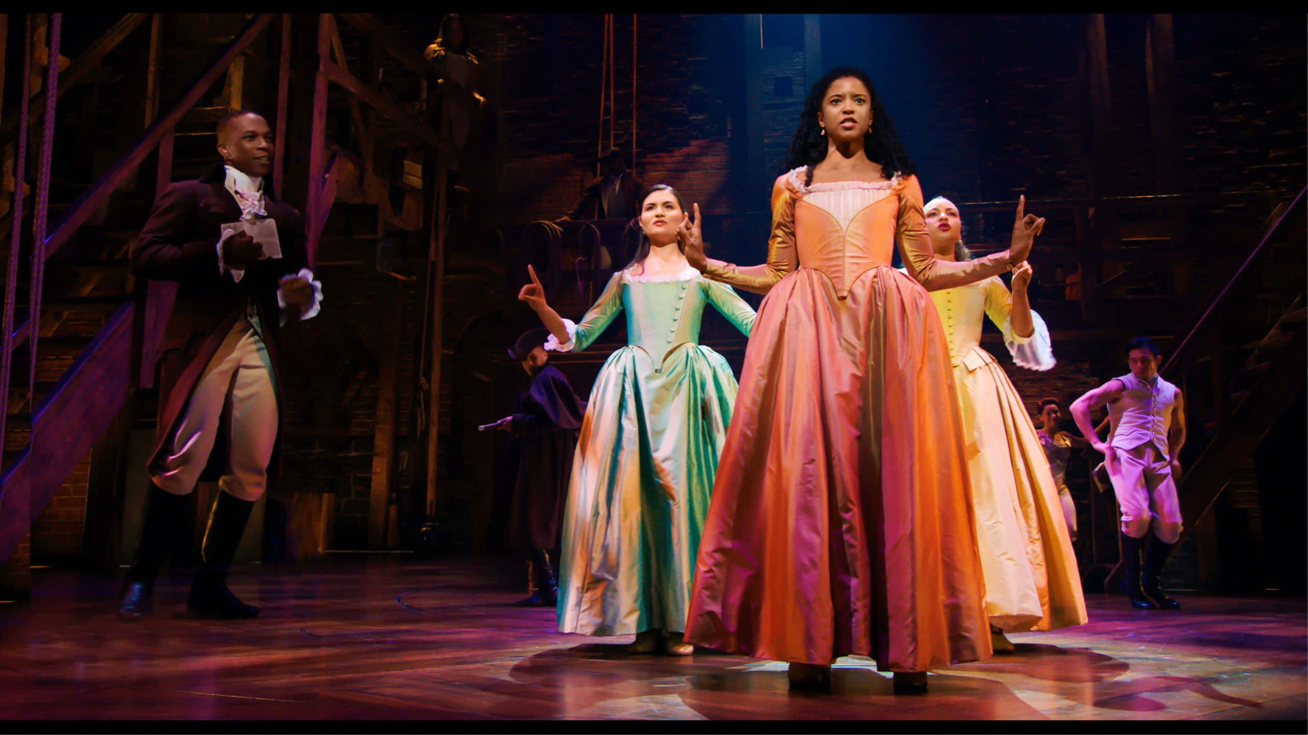 Hamilton 桌布 壁紙 — 劇場表演者穿著精緻的18世紀服裝，在舞台燈光下擺出戲劇性的姿勢。