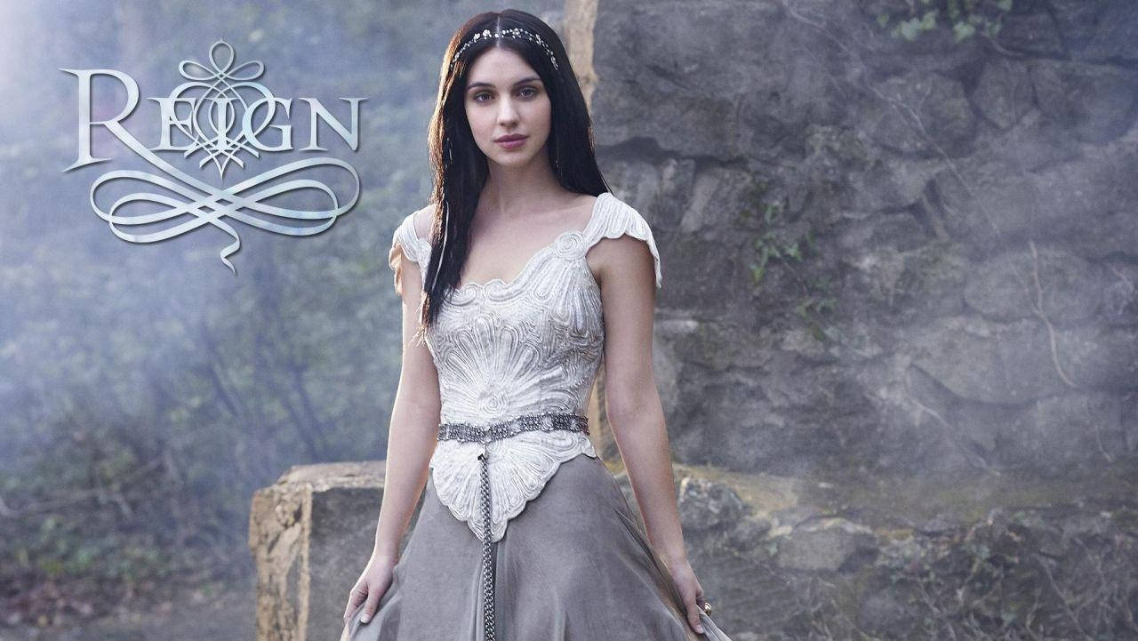劇集《Reign》蘇格蘭女王海報 壁紙 — 一位身穿華麗白色和灰色長袍的女性站在霧氣瀰漫的石牆前，牆上有銀色字體寫著「REIGN」。