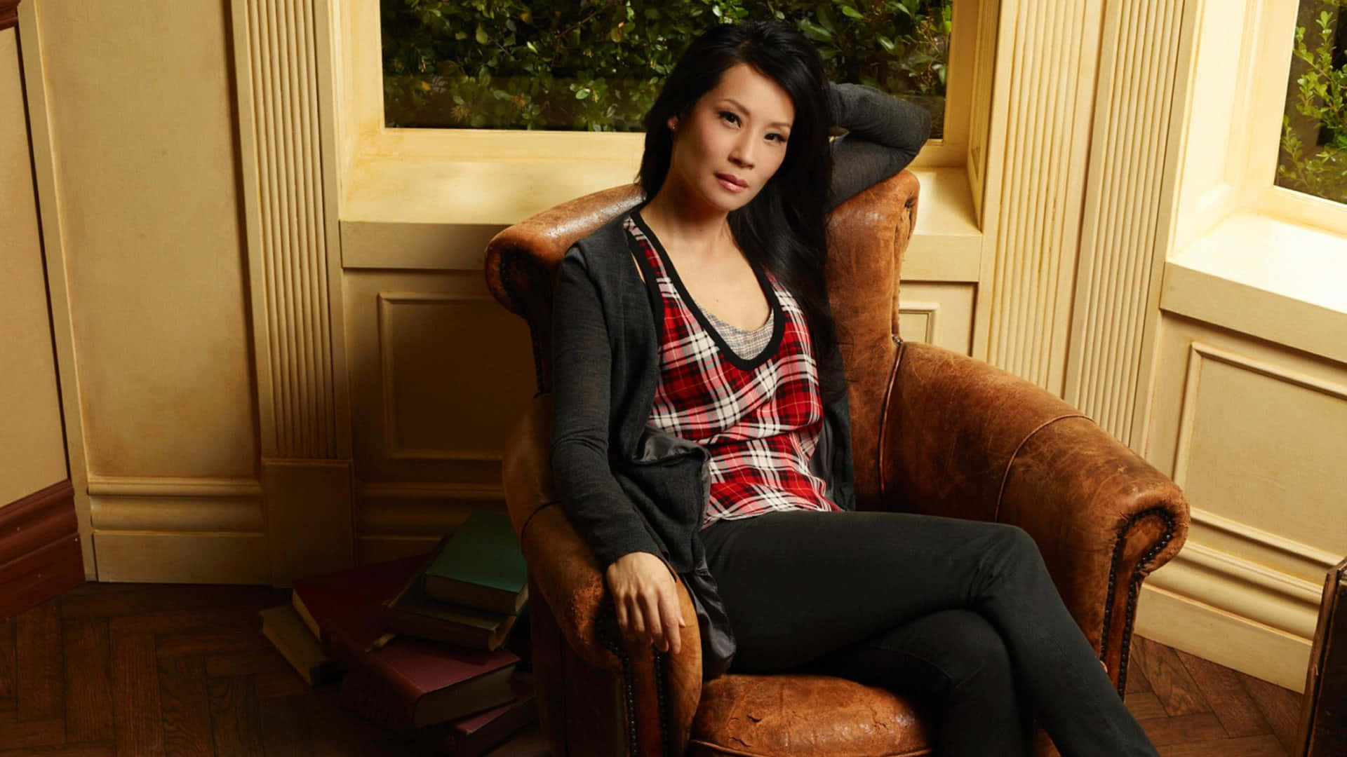 女性坐在室內窗邊的皮革扶手椅上，旁邊有書。