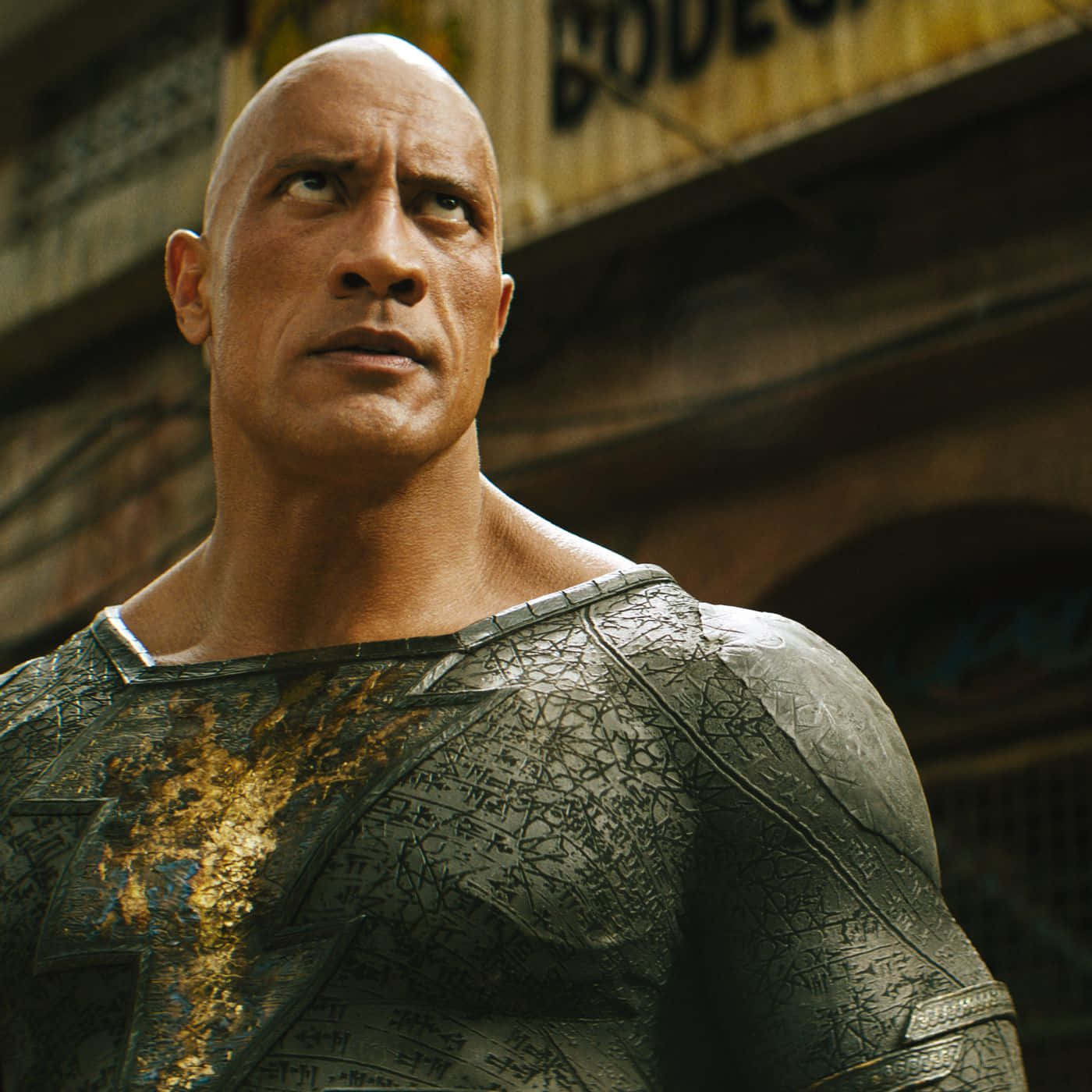 Dwayne Johnson 飾演 Black Adam，身穿破裂盔甲套裝，在破舊小巷中向上看。