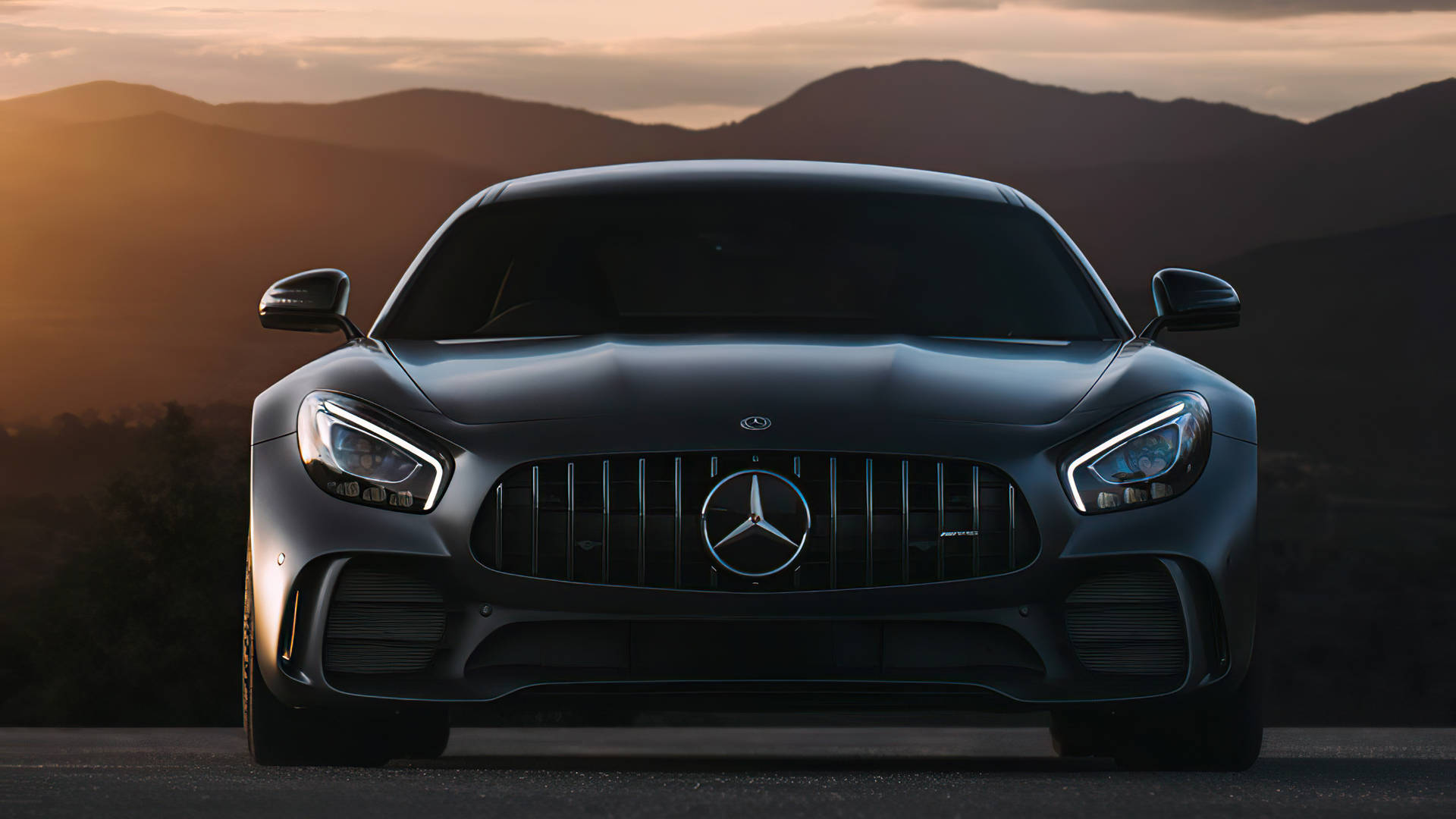 啞光黑色Mercedes-AMG GT在夕陽下對著鏡頭，背景有山脈。