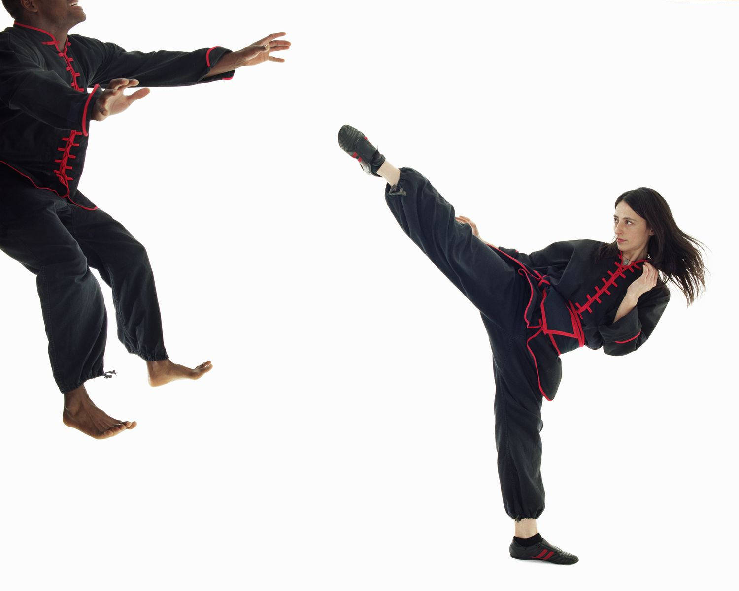 兩名身穿黑紅制服武術家在工作室練習踢腿和格擋。