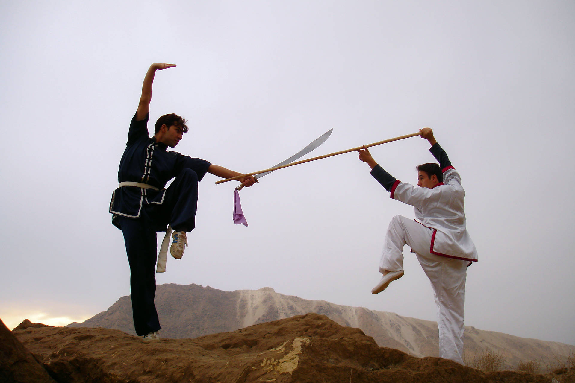兩位武術家在黃昏時分的岩石山上練習劍和棍技巧。