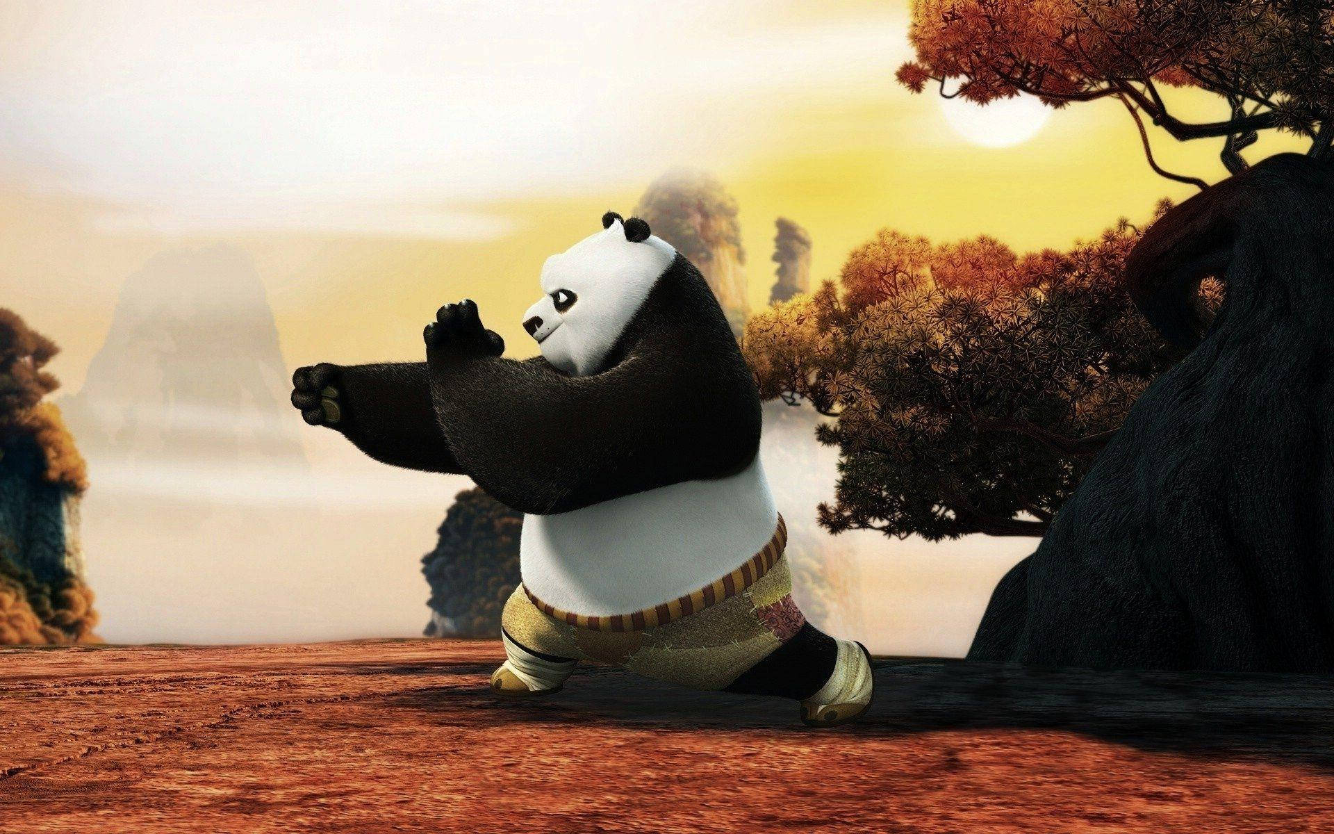 功夫熊貓訓練中 壁紙 — 一隻卡通熊貓在金色日落時分的山徑上擺出武術姿勢，背景有秋樹和霧氣繚繞的山峰。