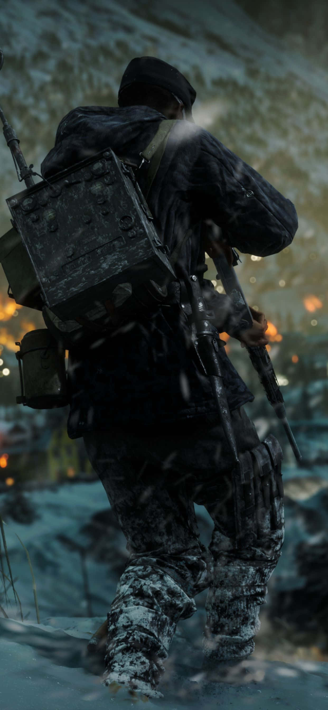 加入《戰地風雲 V》的戰鬥 壁紙 — 一名穿著冬季裝備的士兵帶著步槍和裝備走過雪地，背景中遠處的火光閃爍。