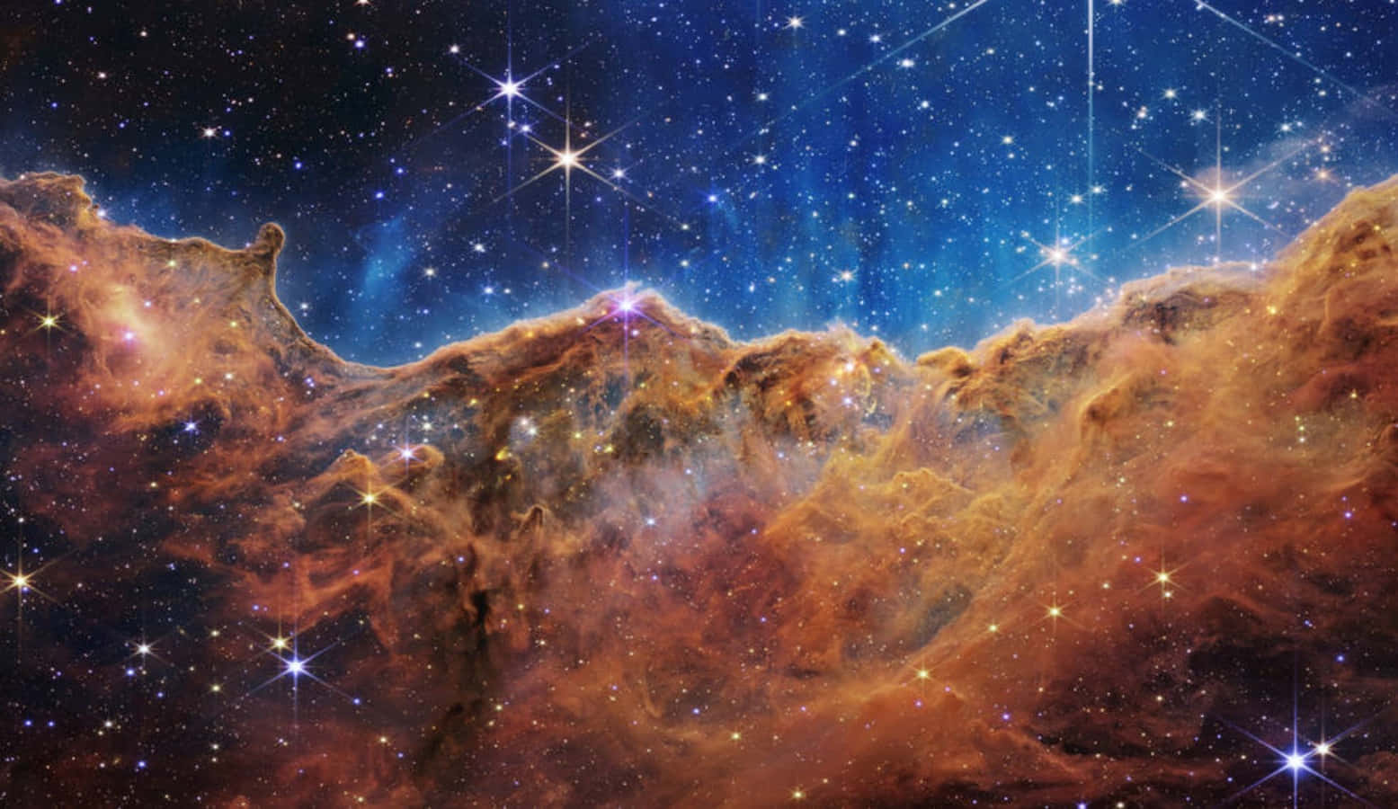 加入探索——超越想像的世界 壁紙 — 廣闊的宇宙星雲，發光的橙色雲朵和閃爍的星星映襯在深藍色的虛空中。