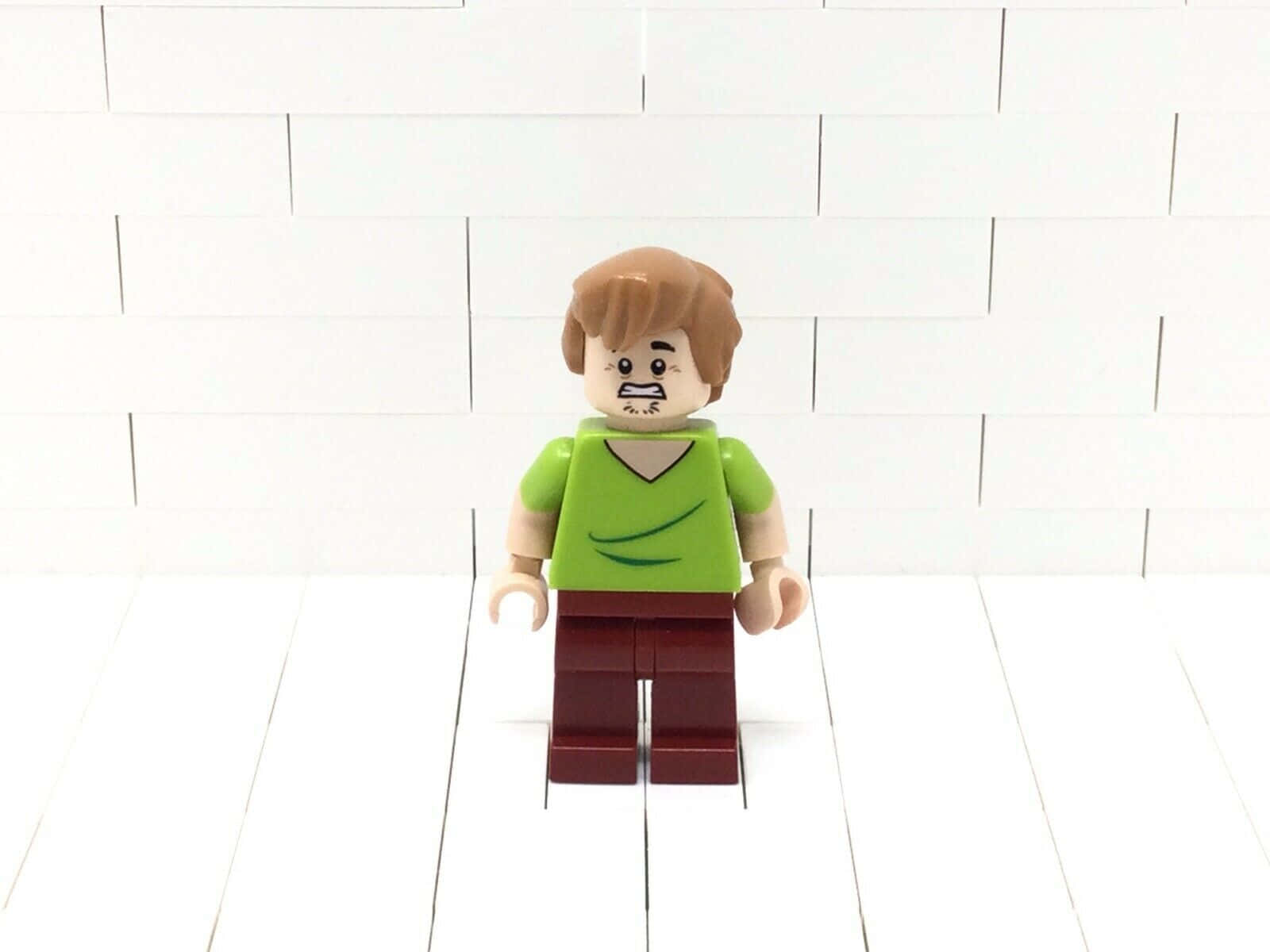 LEGO弗雷德·弗林斯通人仔喺白色磚背景前擺出唔開心嘅樣。