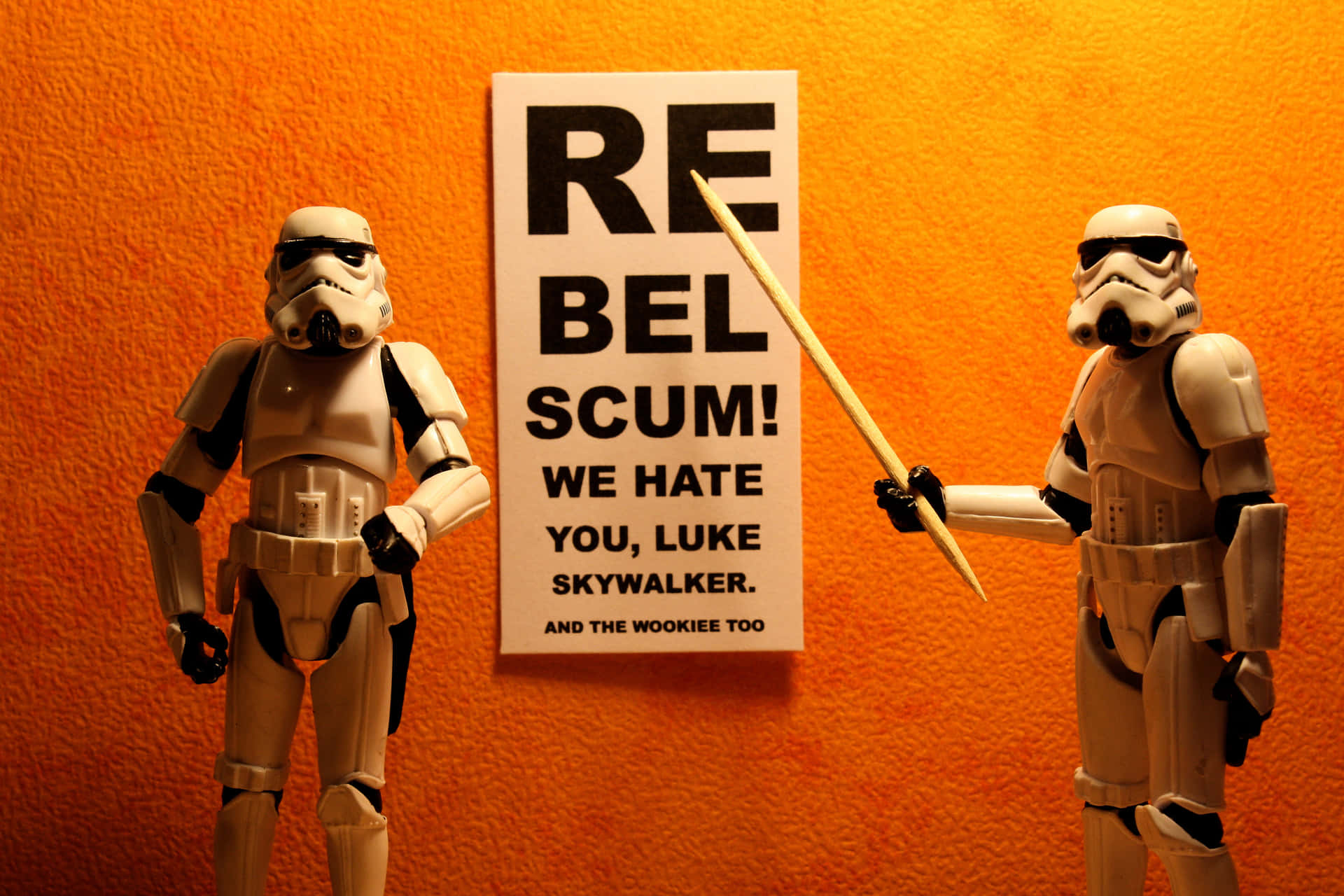 兩個風暴兵可動人偶站在一個橙色牆壁前，旁邊有一個寫著「Rebel Scum!」的標語牌。