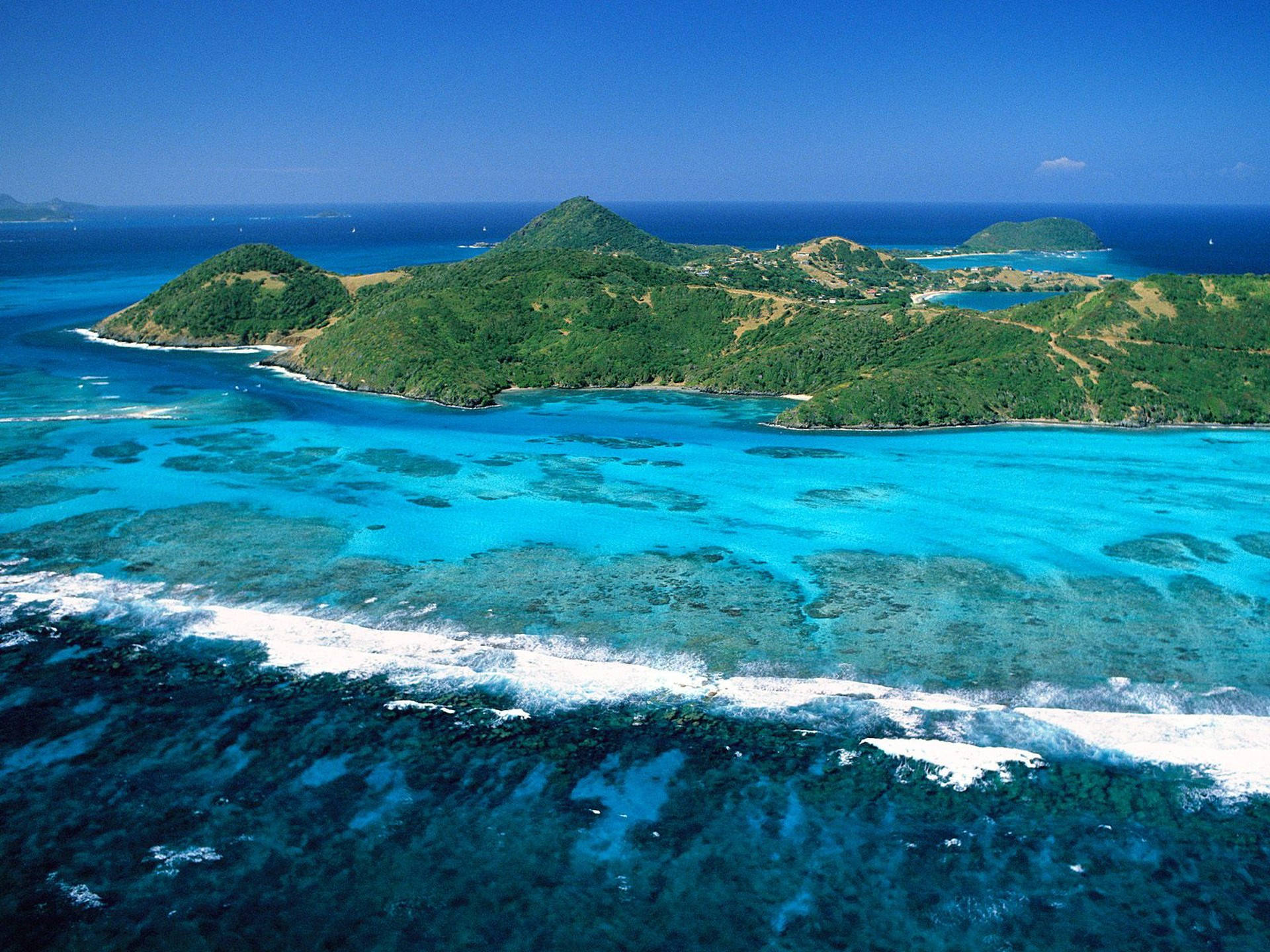 加勒比海風景 壁紙 — 從高空俯瞰，鬱鬱蔥蔥的綠色島嶼被充滿活力的碧綠海水和珊瑚礁環繞，上方是清澈的藍天。