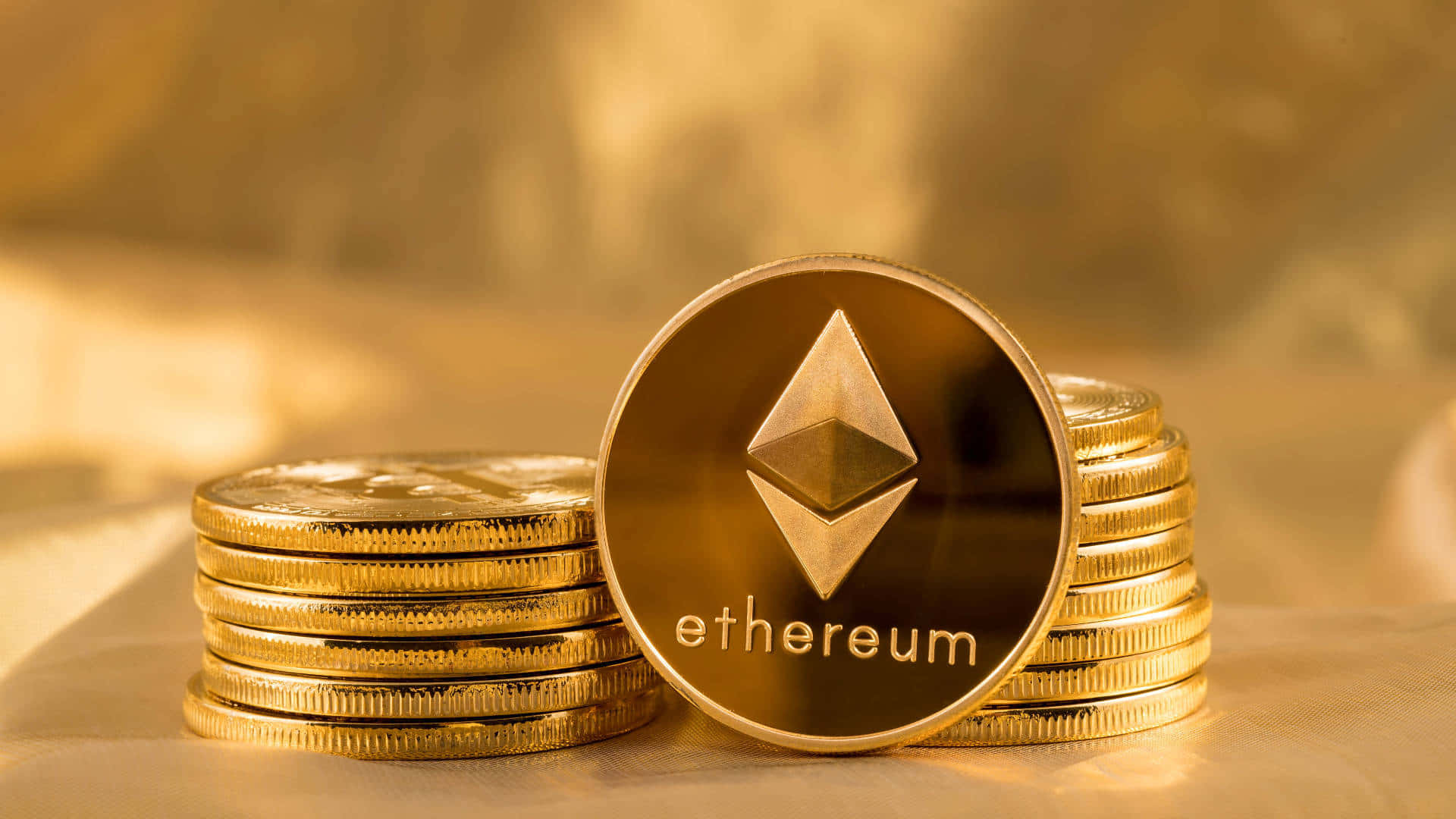 加密以太坊金幣 壁紙 — 一枚閃閃發光的金色以太幣直立在一堆類似硬幣旁邊，沐浴在溫暖的金色光線下。