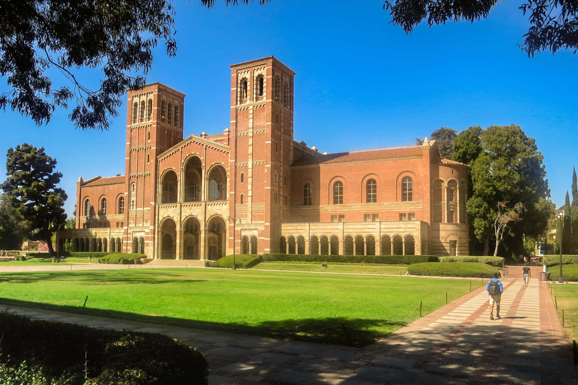 學生們沿著小路走向一座歷史悠久的大學建築，該建築有紅磚塔和綠色草坪。
