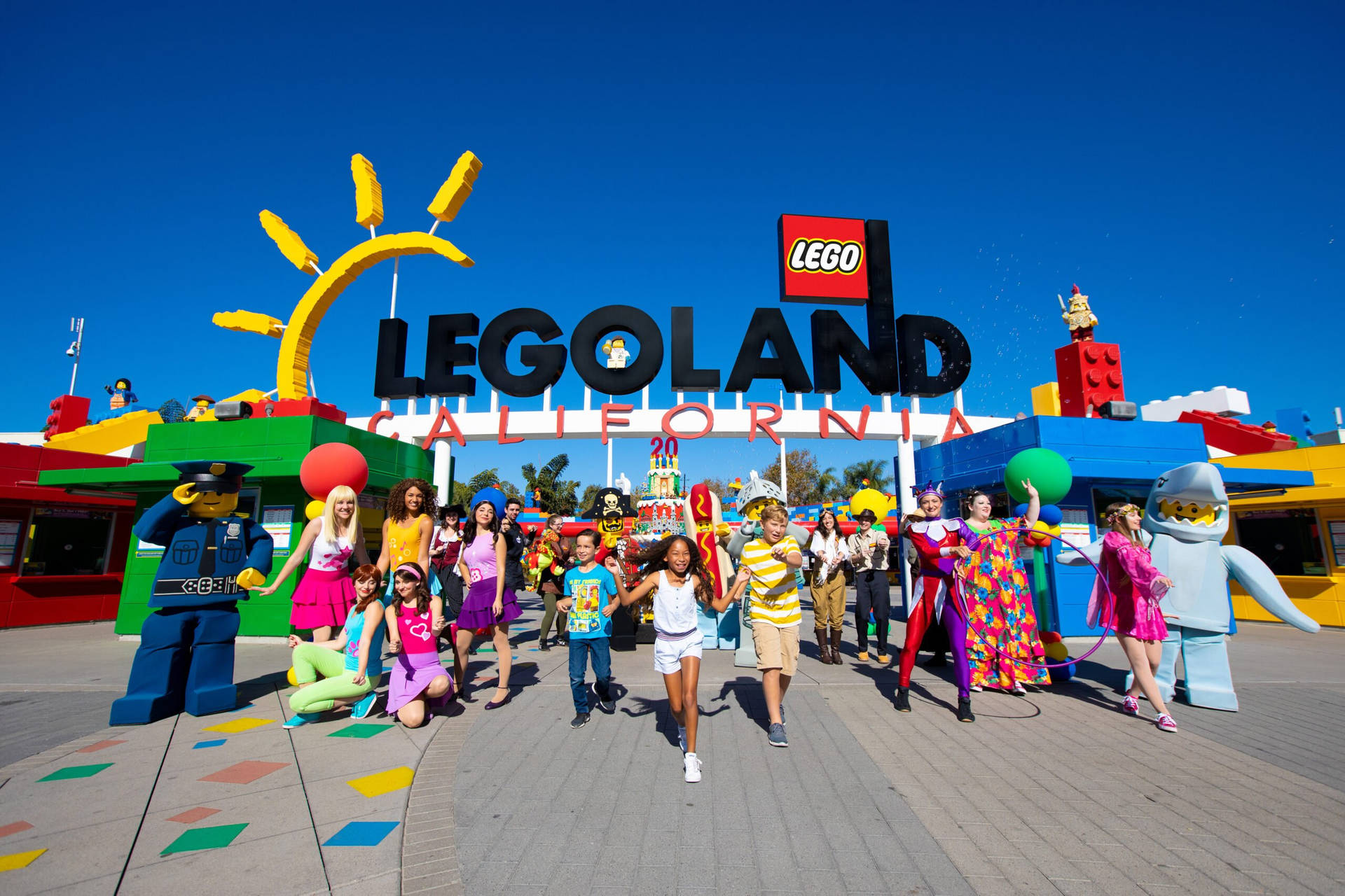 在陽光明媚的日子裡，孩子們和LEGO角色在LEGOLAND California入口處微笑。