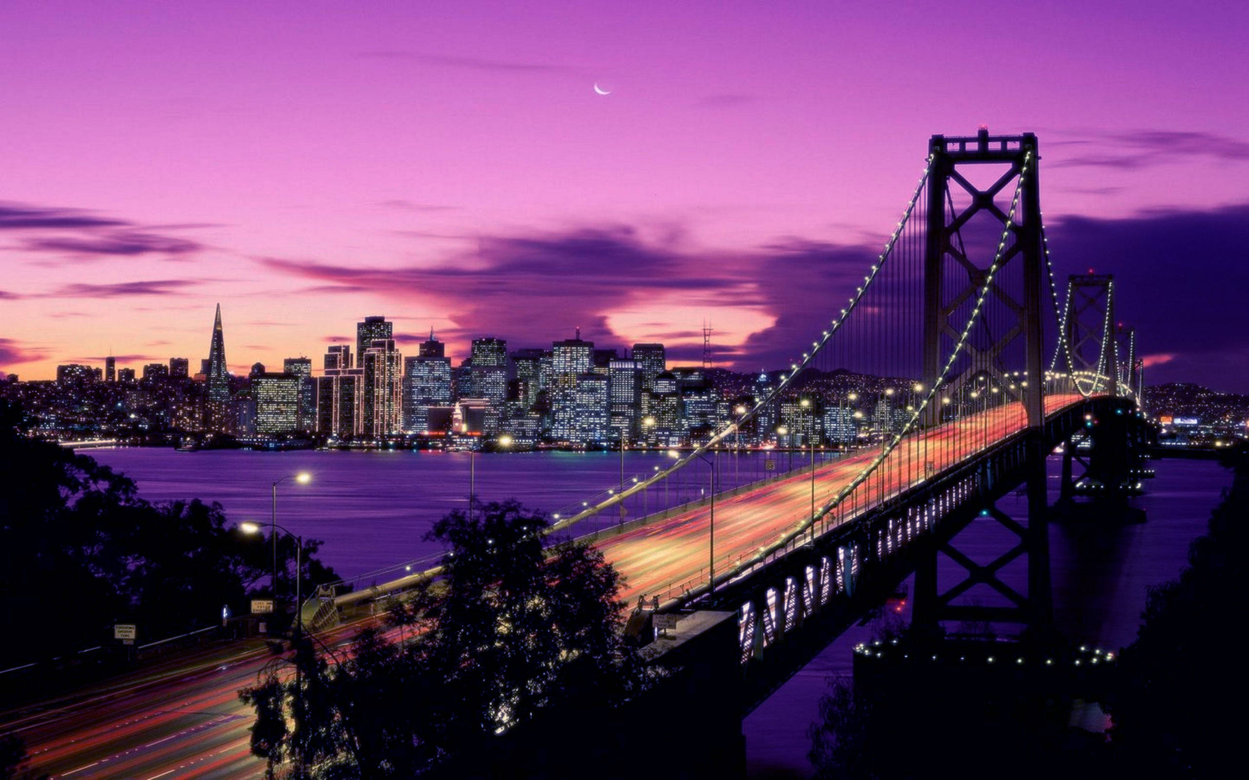 加州金門大橋夜景 壁紙 — 充滿活力的紫色日落照亮了舊金山的天際線和海灣大橋，車流的光線條紋。