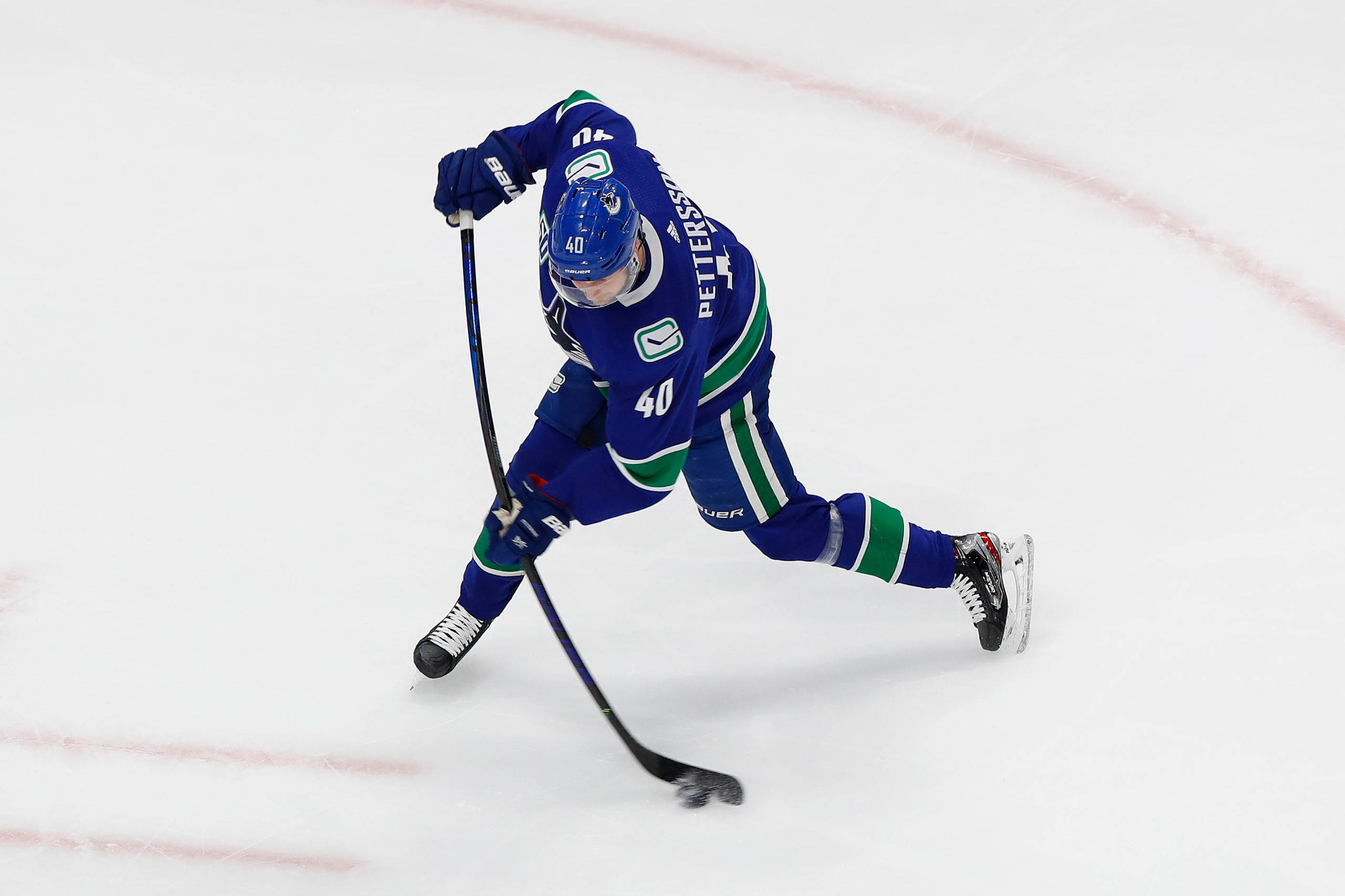 加拿大NHL球員埃利亞斯·佩特ters森穿藍色球衣 壁紙 — 一名身穿藍綠球衣的冰球運動員在比賽中低身俯在冰上，手持球棍。