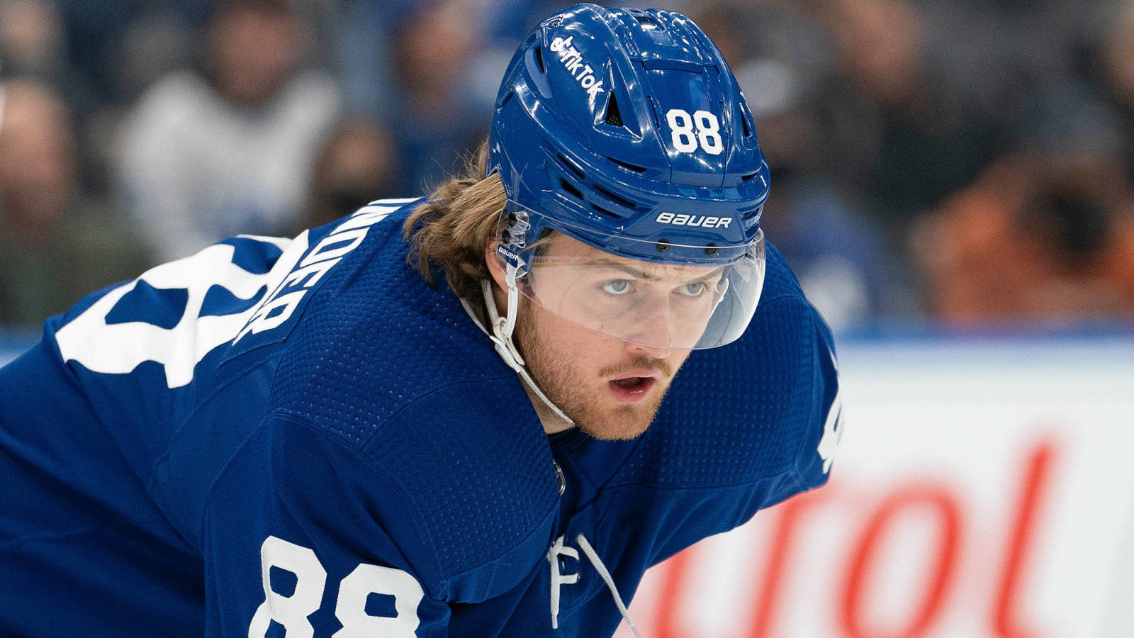 加拿大NHL球員威廉·尼蘭德肖像照（Nick Turchiaro攝） 壁紙 — 一名專注的冰球運動員身穿藍色多倫多楓葉隊球衣，在比賽中於冰上向前傾身。