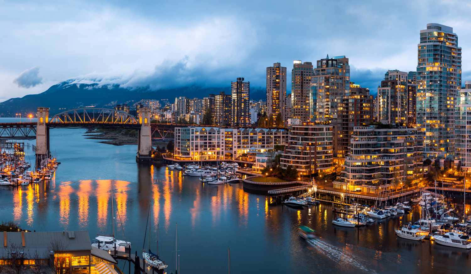 黃昏城市景觀，多雲天空下，水面上有發光的建築物和船隻。