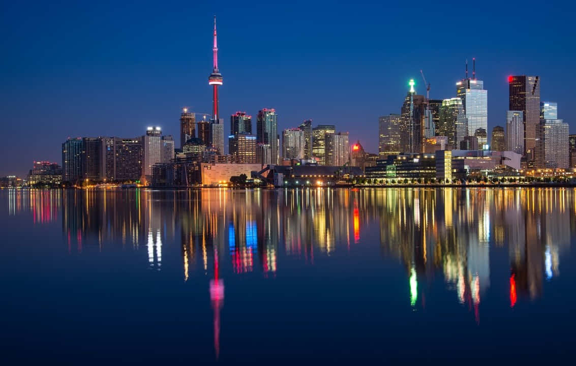 多倫多城市天際線夜景，燈火通明的建築物倒映在水中。