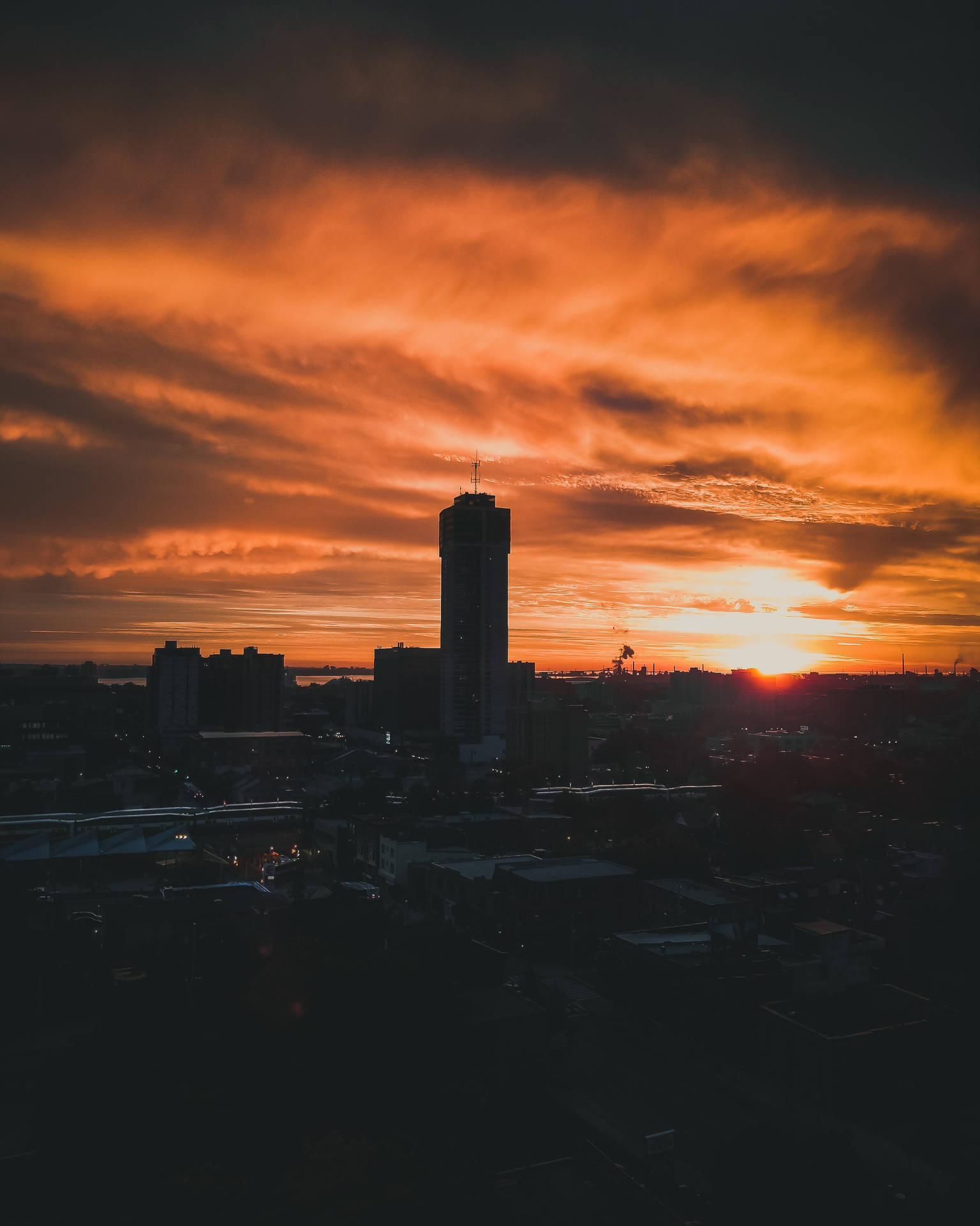 日落時分的城市天際線，一座高樓在火熱的橙色雲層中形成剪影。