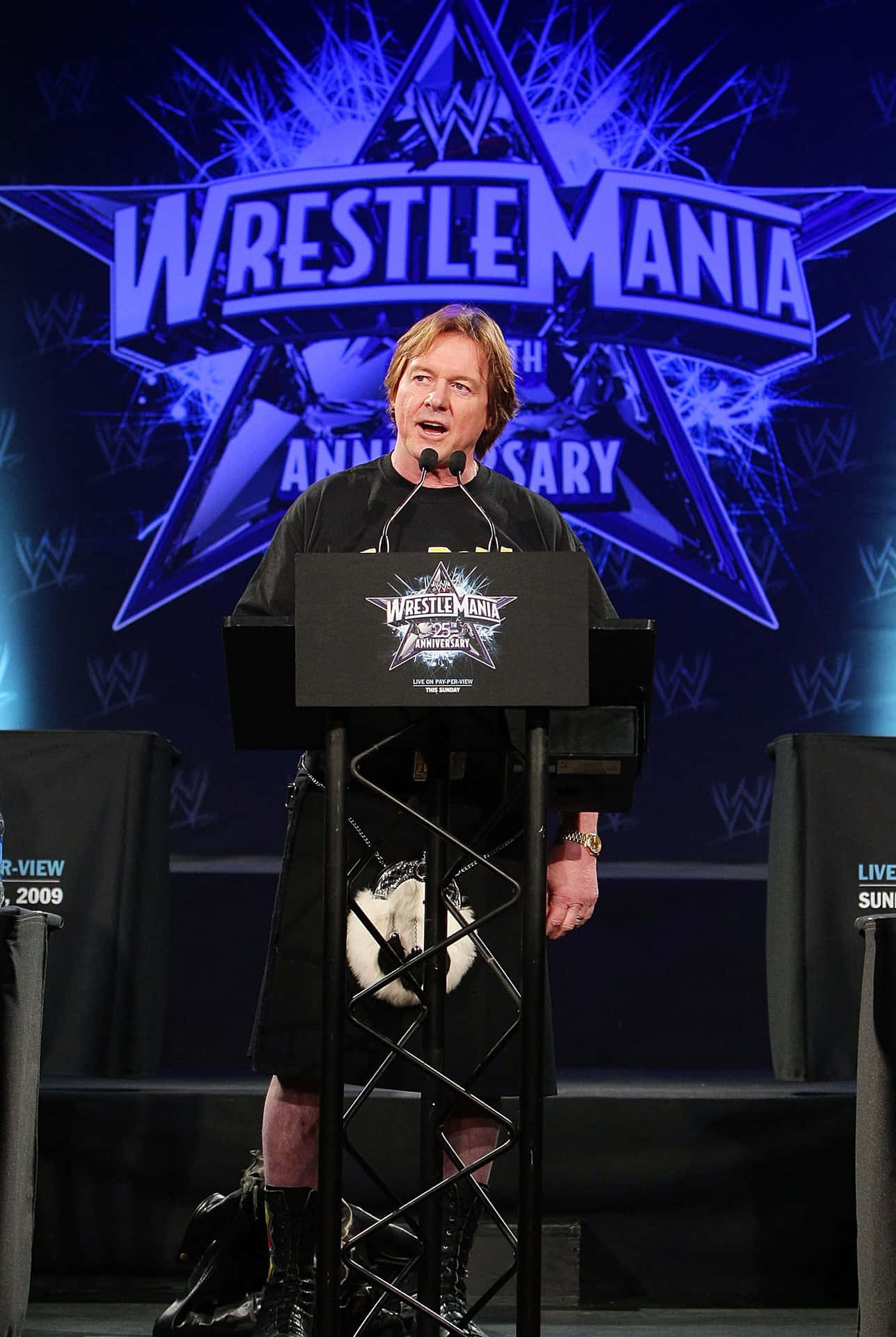 穿著蘇格蘭裙的男子在WrestleMania記者會講台上發言。