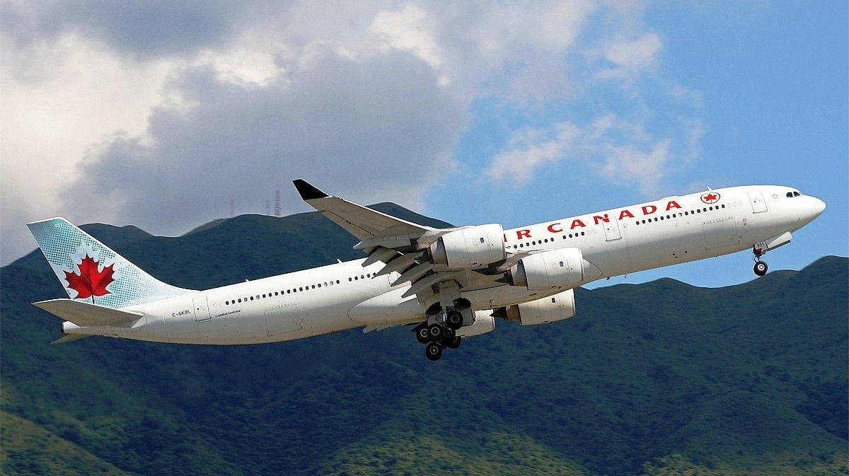 加拿大航空飛機在藍天白雲下，降落在綠色山脈之上。