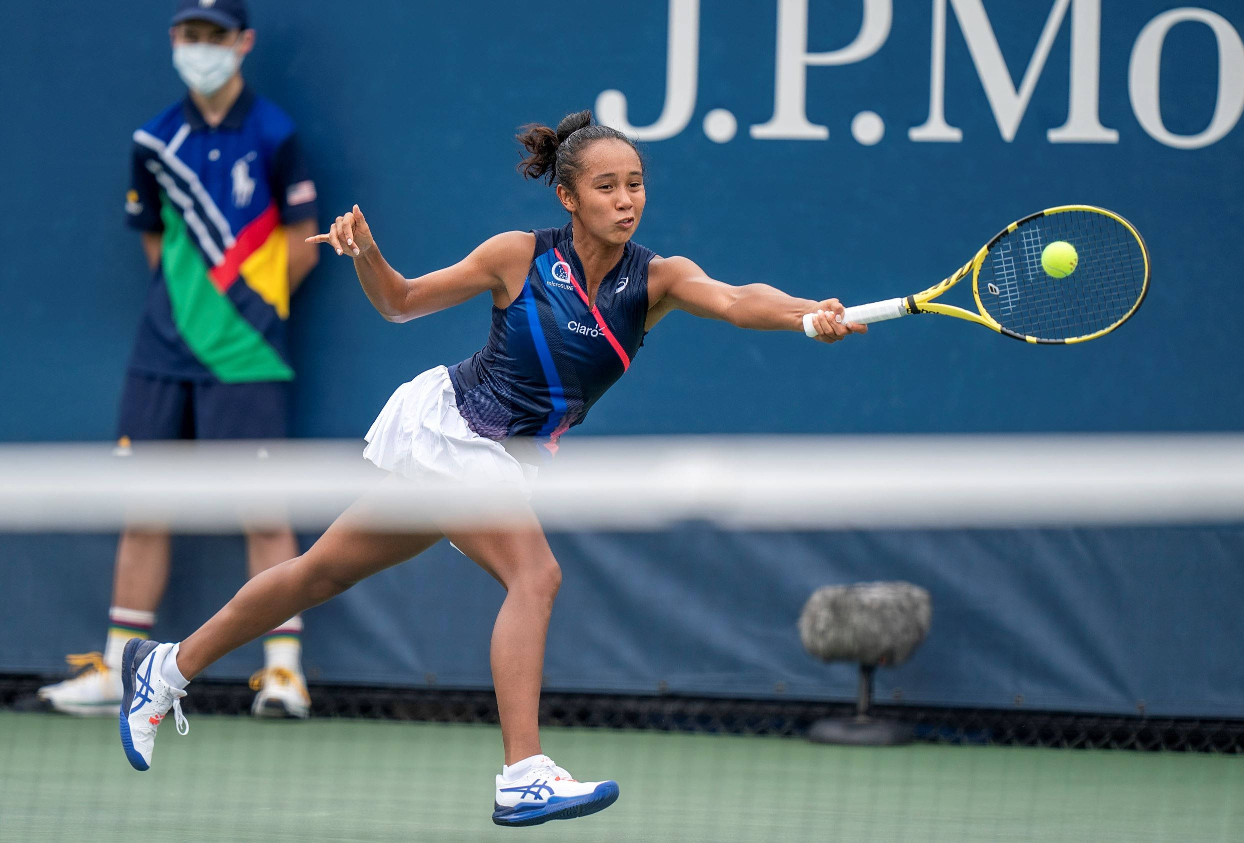 加拿大選手萊拉·費爾南德斯於美國公開賽 壁紙 — 一名女網球運動員在揮拍中途向前猛衝，在綠色球場上擊打一個黃色球，身後有一面藍色牆壁。