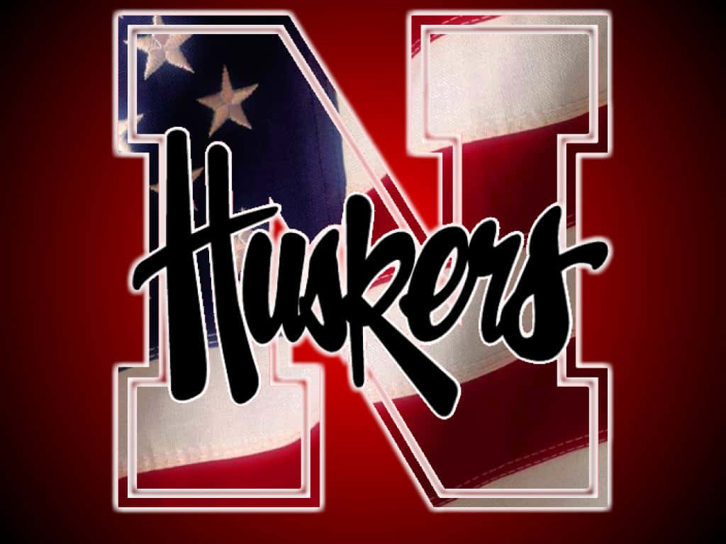 加油，大紅隊！ 壁紙 — 大膽的黑色 'Huskers' 字體覆蓋在一個大型風格化 'N' 上，該 'N' 填充了美國國旗布料，背景為深紅色。