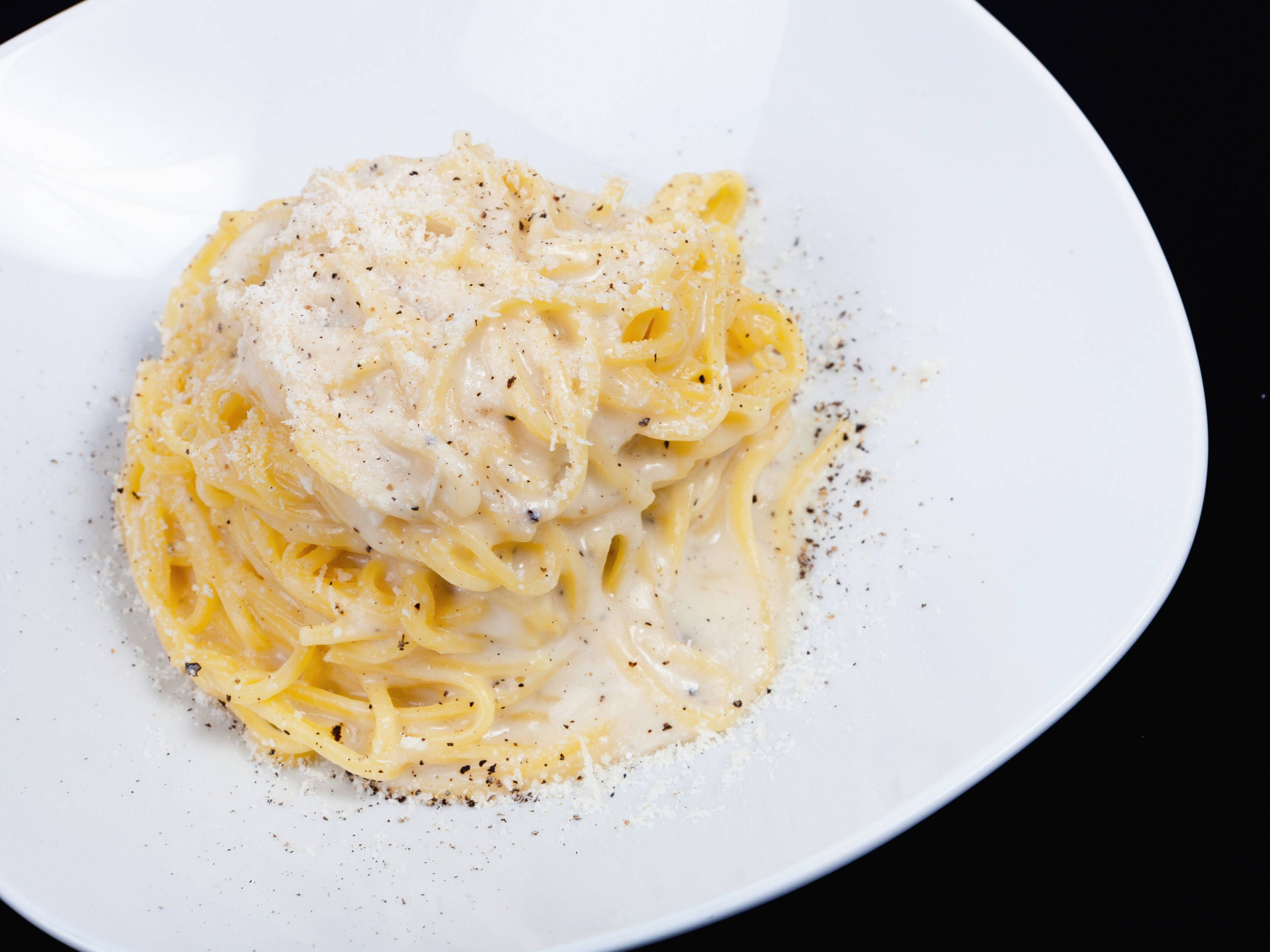 加濃奶油的 Cacio E Pepe 壁紙 — 一碟忌廉卡邦尼意粉，配上磨碎芝士和黑胡椒，放在白色碟上，黑色背景。