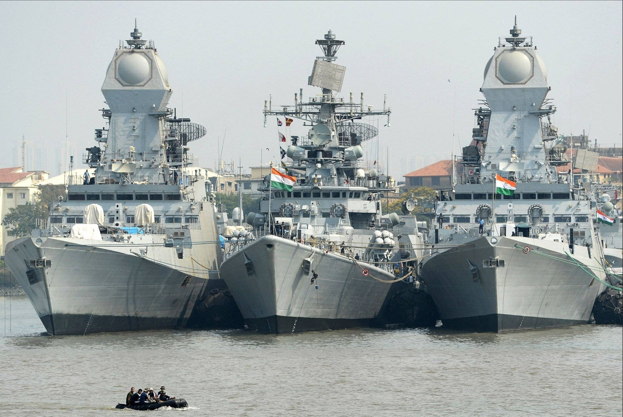 加爾各答三艘船 壁紙 — 三艘大型印度海軍軍艦並排停泊在港口，附近有一艘載有人員的小型充氣艇。