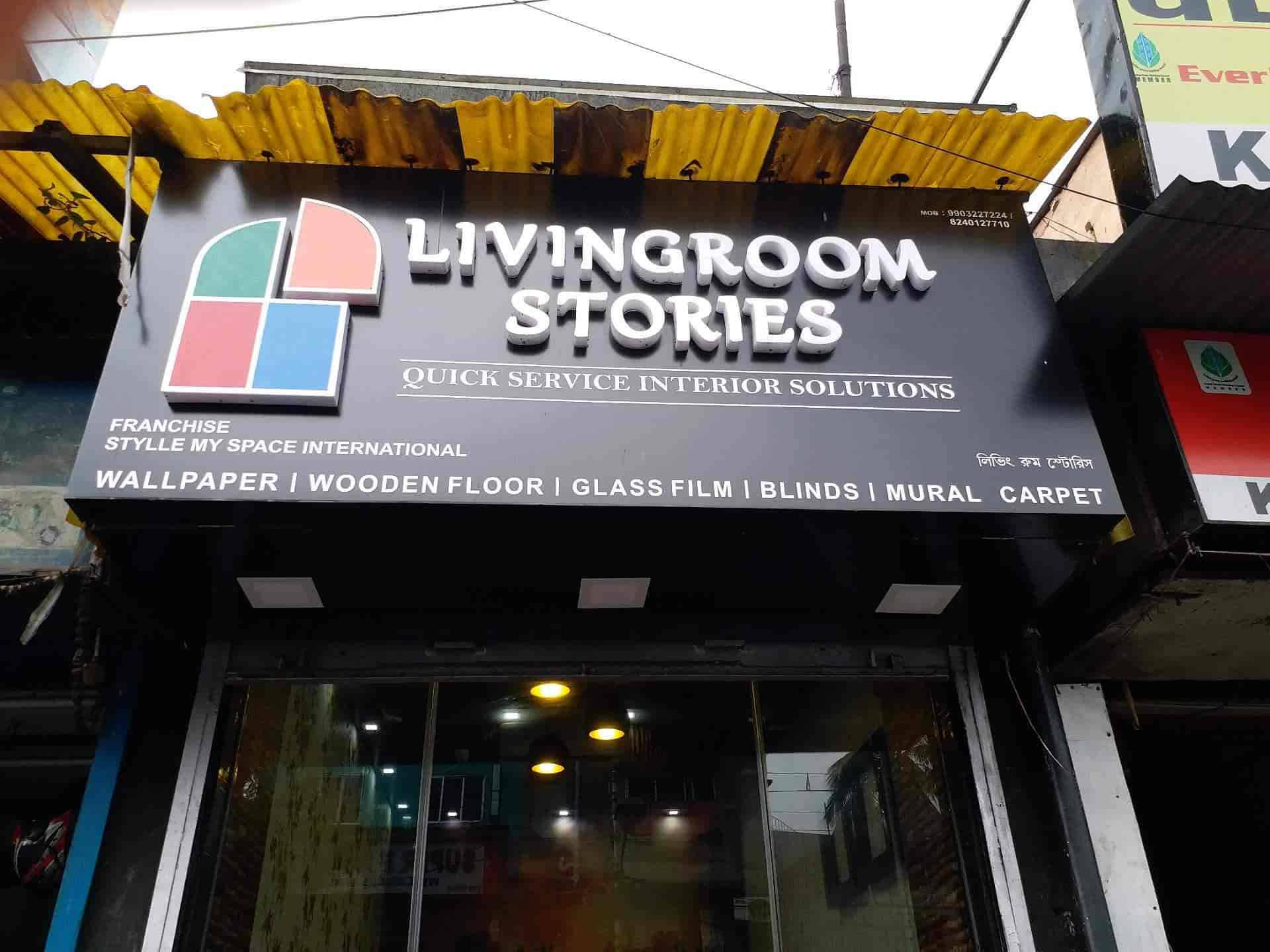 加爾各答客廳故事 壁紙 — 一個黑色嘅店舖招牌，上面寫住「Livingroom Stories」，有色彩繽紛嘅幾何標誌同白色文字，喺黃色波浪形簷篷下宣傳室內設計方案。