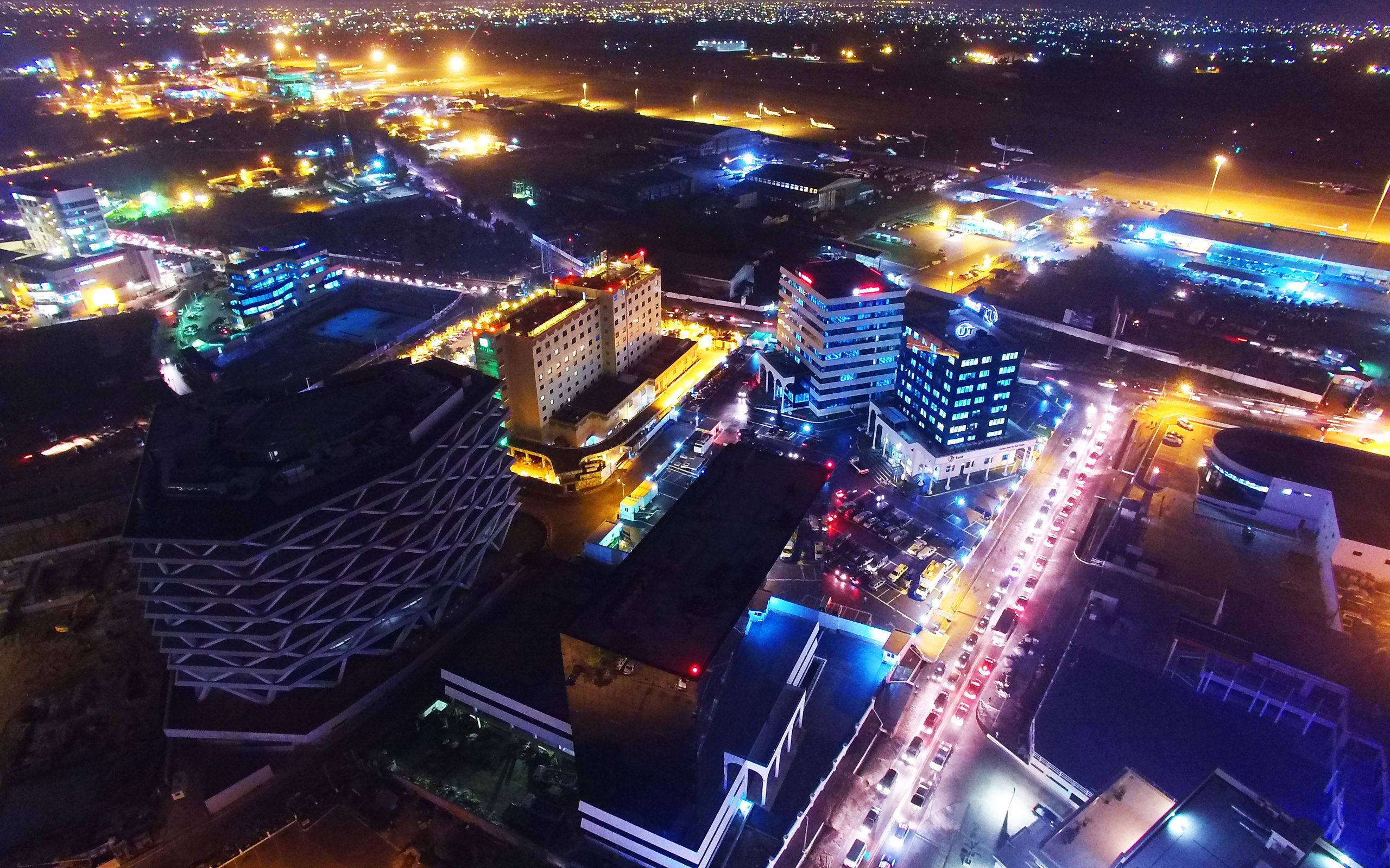 加納商業區夜景 壁紙 — 充滿活力城市景觀的空中夜景，建築物閃閃發光，繁忙街道上佈滿車燈。