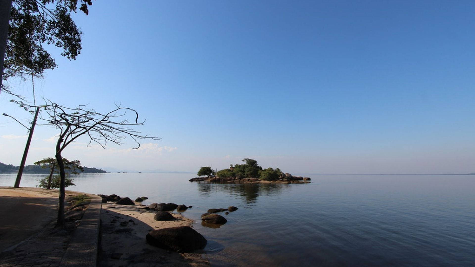 加納沃爾塔湖 壁紙 — 寧靜的湖邊景色，藍天白雲下有一個小樹島。