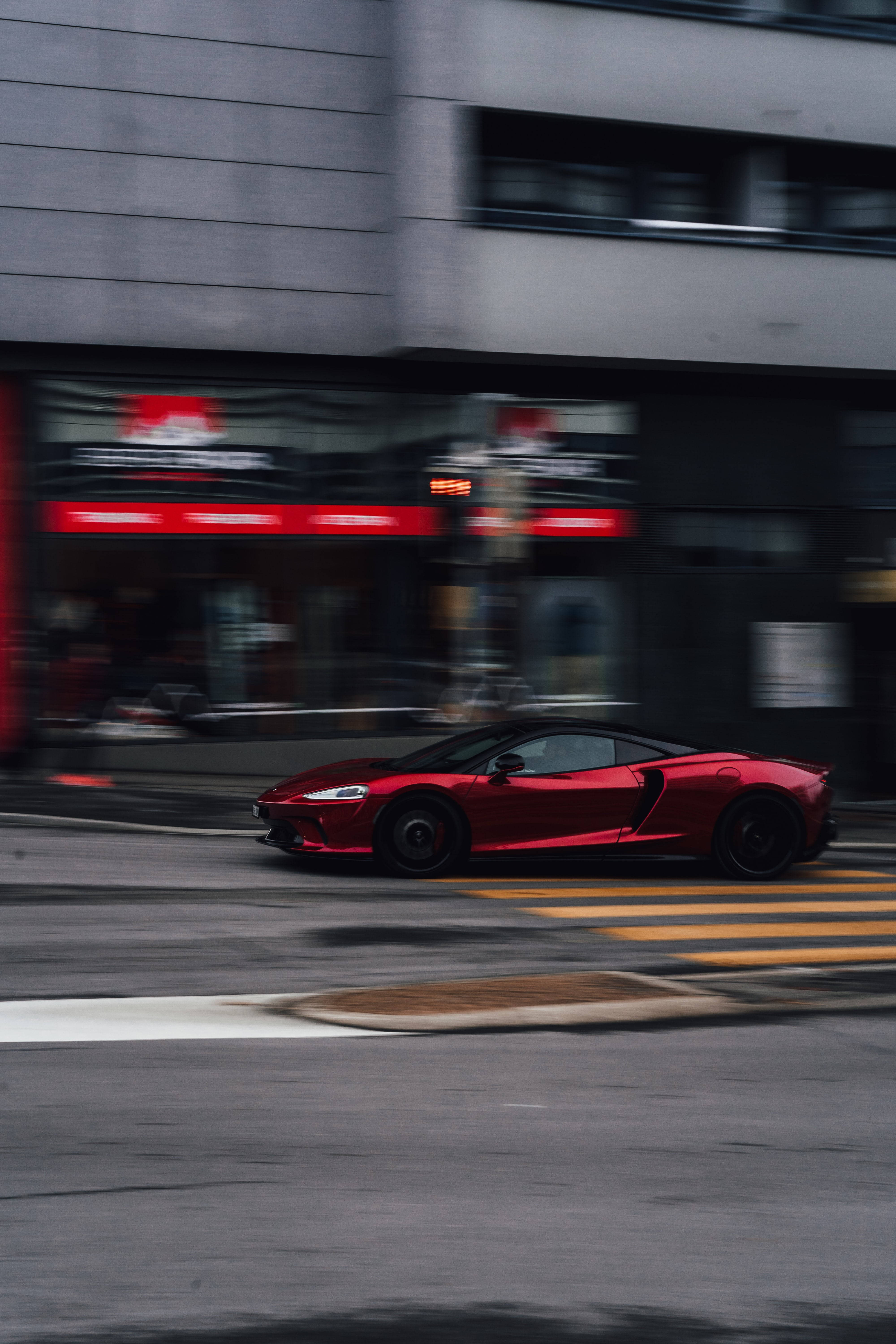 加速中的紅黑跑車 壁紙 — 一輛鮮紅色跑車在城巿街道上飛馳，動態模糊效果劃過城巿背景。