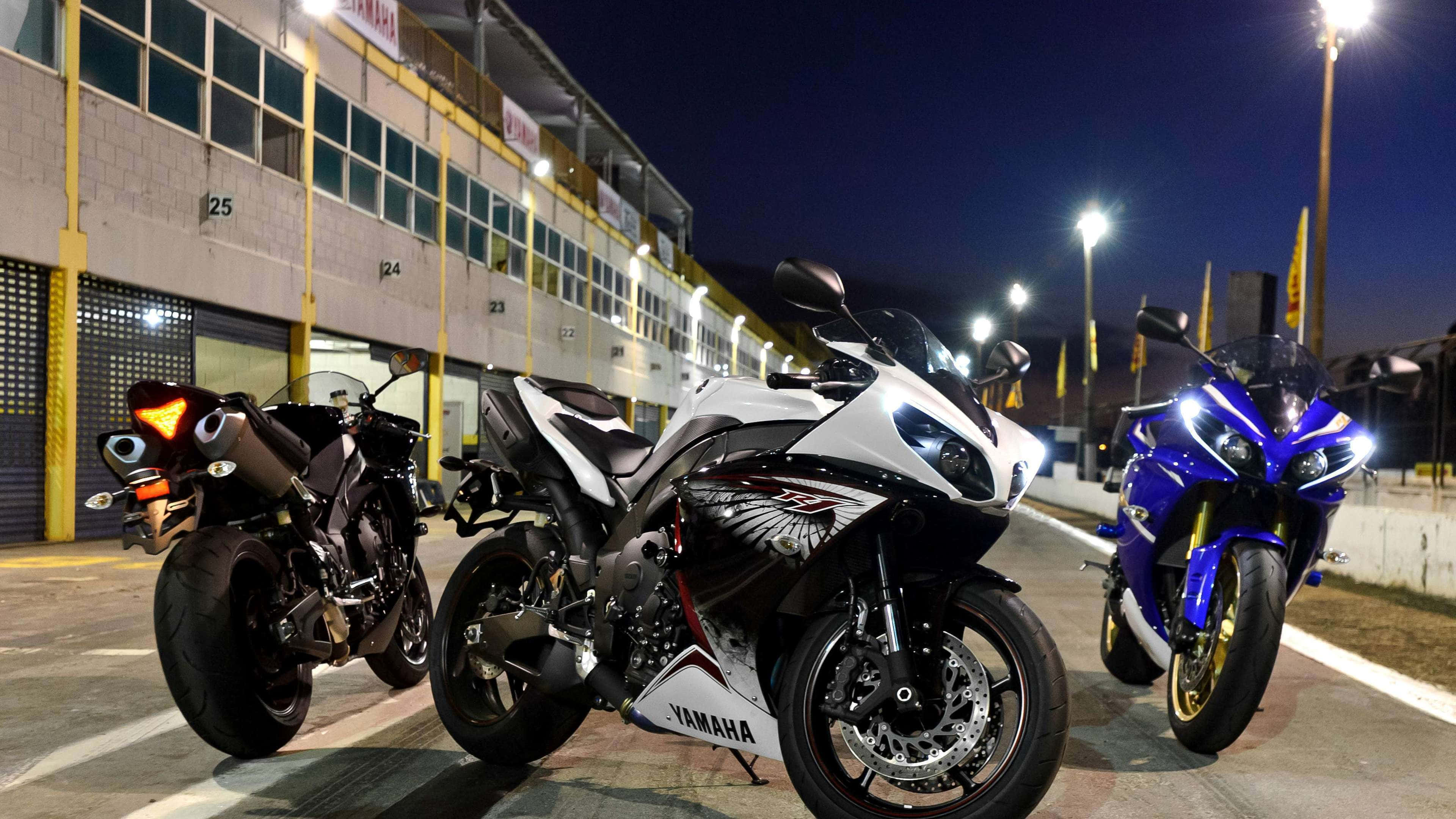 加速你的騎行體驗！4K自行車 壁紙 — 三輛高性能Yamaha跑車在夜間停泊在賽車設施外，在明亮的泛光燈下閃閃發光。