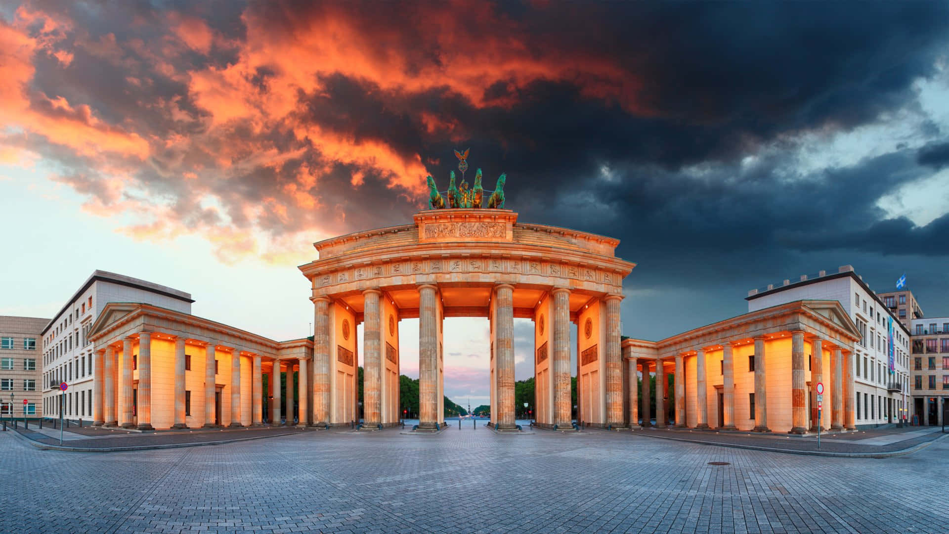 Germany 桌布 壁紙 — 勃蘭登堡門沐浴在金色的夕陽光芒中，上方是火紅的橙色雲彩，下方是空無一人的鵝卵石廣場。