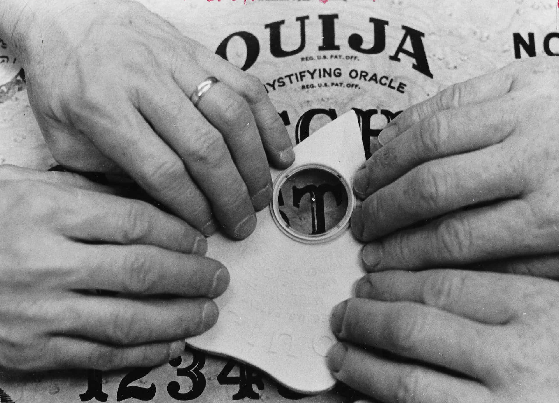 四隻手喺字母上面揸住 Ouija 板嘅指示器。