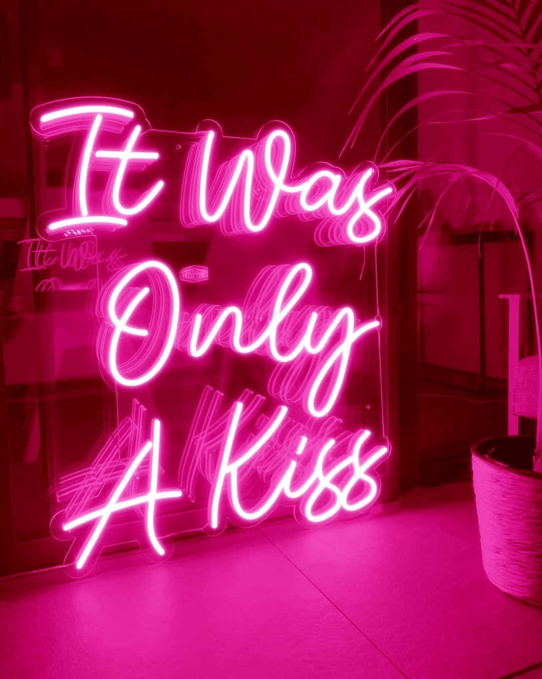 粉紅色霓虹燈牌，上面寫著「It Was Only A Kiss」，在一個有植物的舒適房間裡。