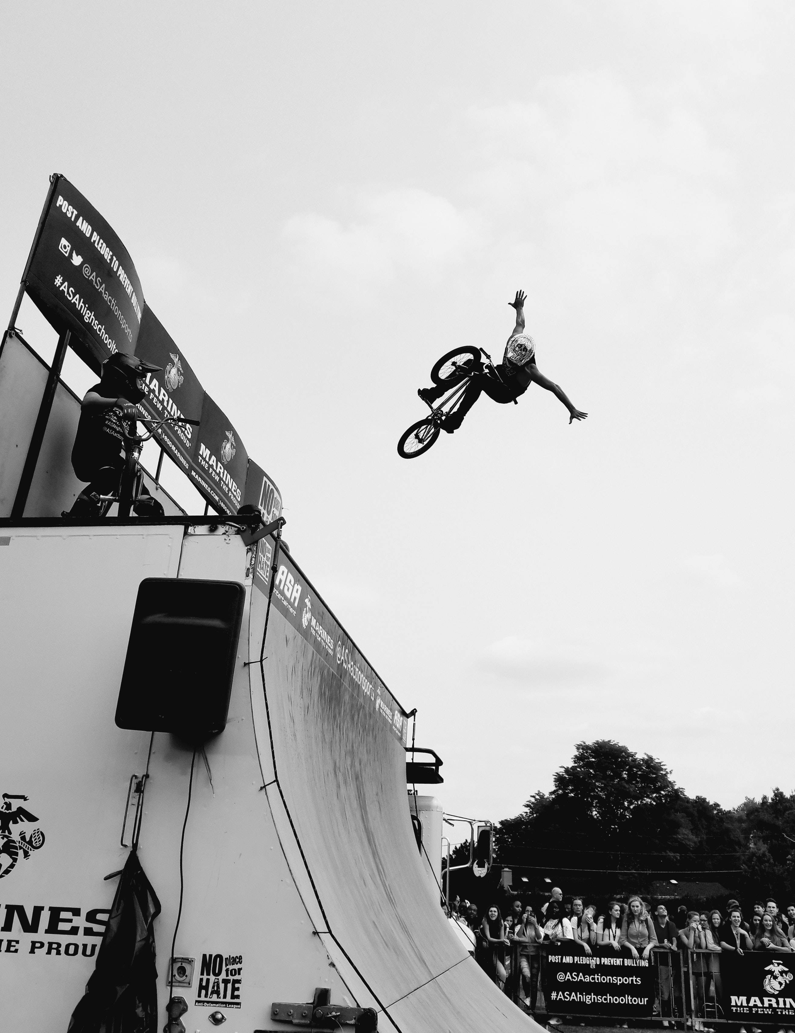 勇敢的BMX自行車手 壁紙 — 一名BMX車手在斜坡上方騰空飛翔，觀眾從下方觀看，黑白動作鏡頭。