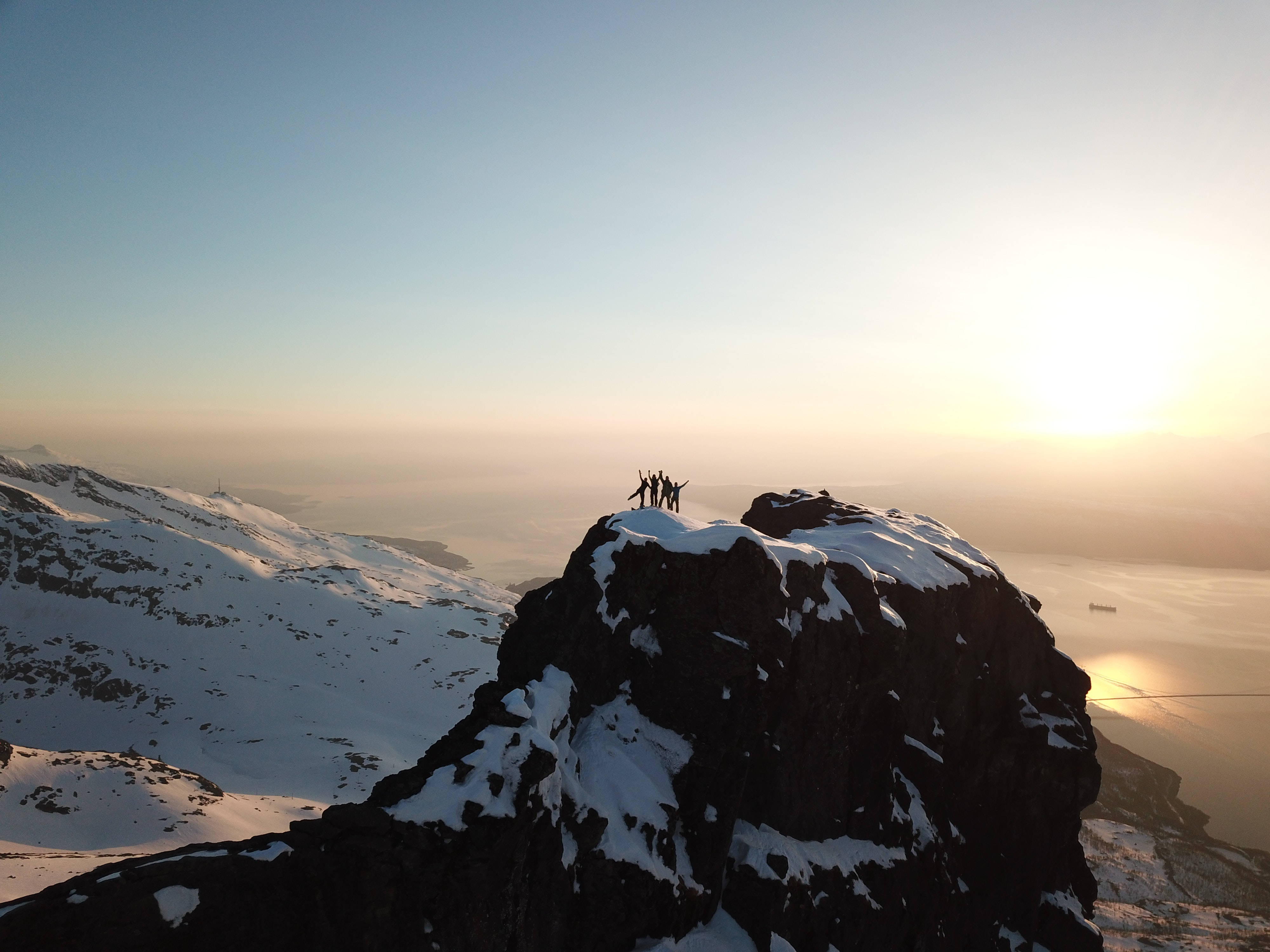 勇敢的寒風友伴 壁紙 — 剪影的登山者在白雪覆蓋的山頂慶祝，金色的日出在下方霧氣繚繞的峽灣上閃耀。