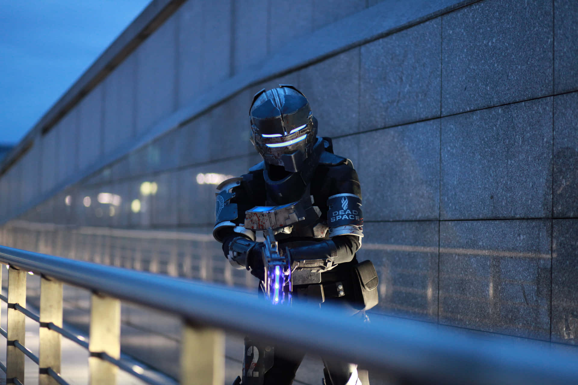 一位穿著 Dead Space 角色扮演服裝的人，在夜間靠近欄杆手持發光武器。