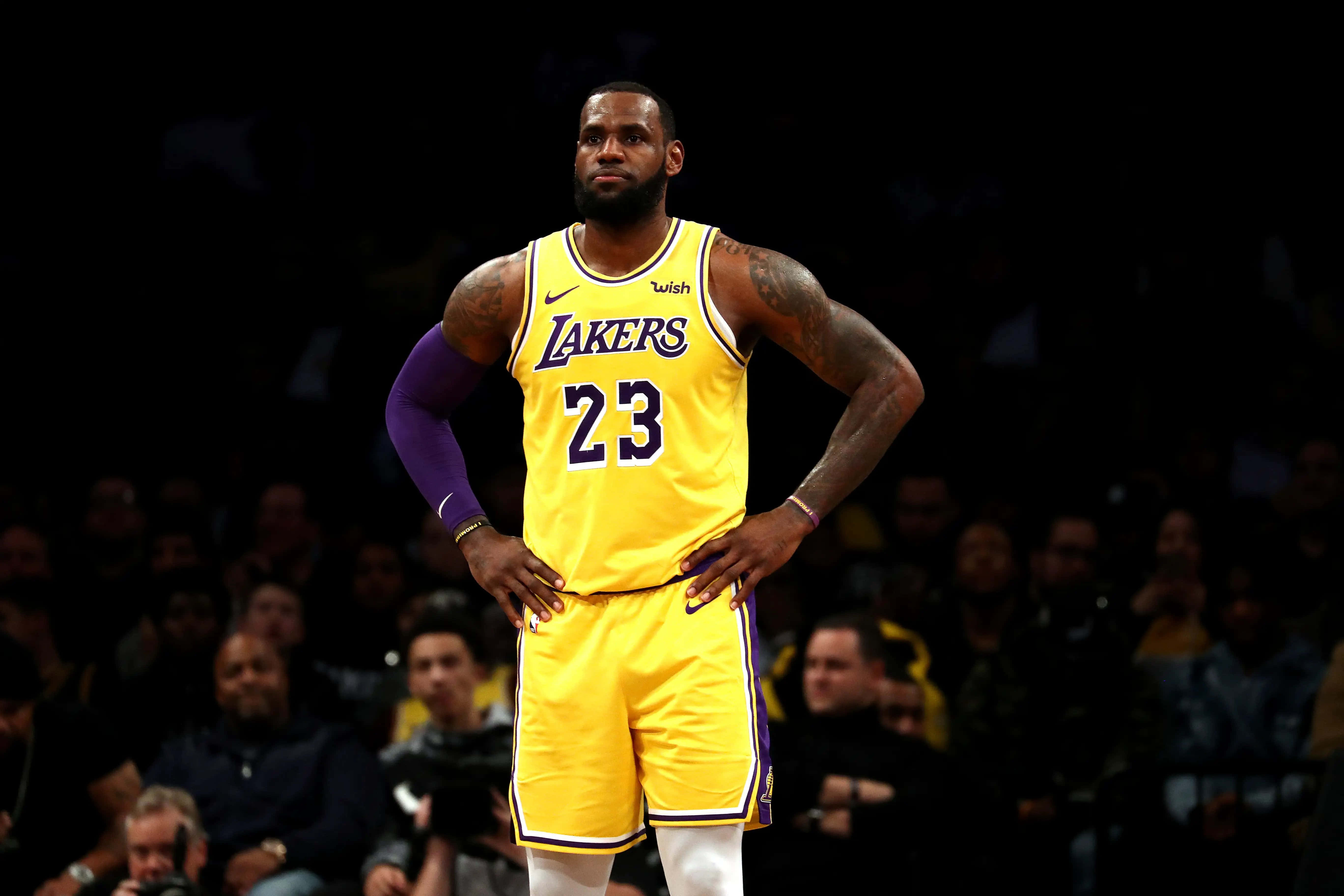 勒布朗·詹姆斯在NBA總決賽中再現灌籃風采 壁紙 — 勒邦占士身穿黃色湖人球衣，在場館燈光下自信地雙手叉腰站立。