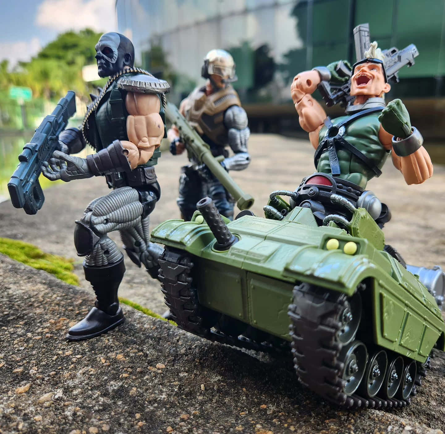 動作人偶對戰場景 壁紙 — 三個穿著軍裝的動作人偶在戶外岩石表面上與一輛綠色坦克戲劇性地擺姿勢。