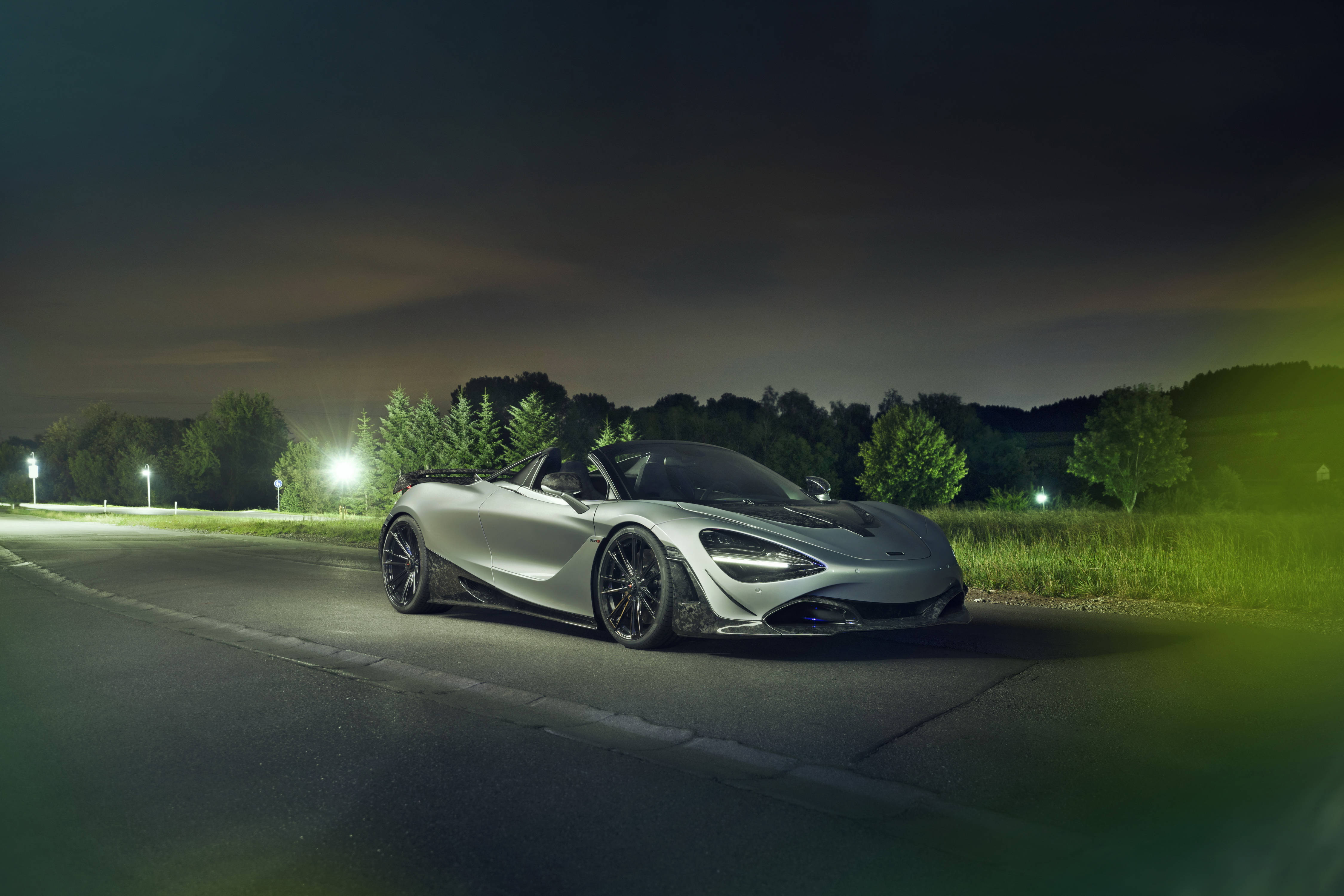 動感優雅：麥拉倫720S豪華超跑 壁紙 — 一輛時尚的銀色McLaren Speedtail開篷車在寧靜的鄉村道路上，樹木環繞，在夜燈下閃閃發光。