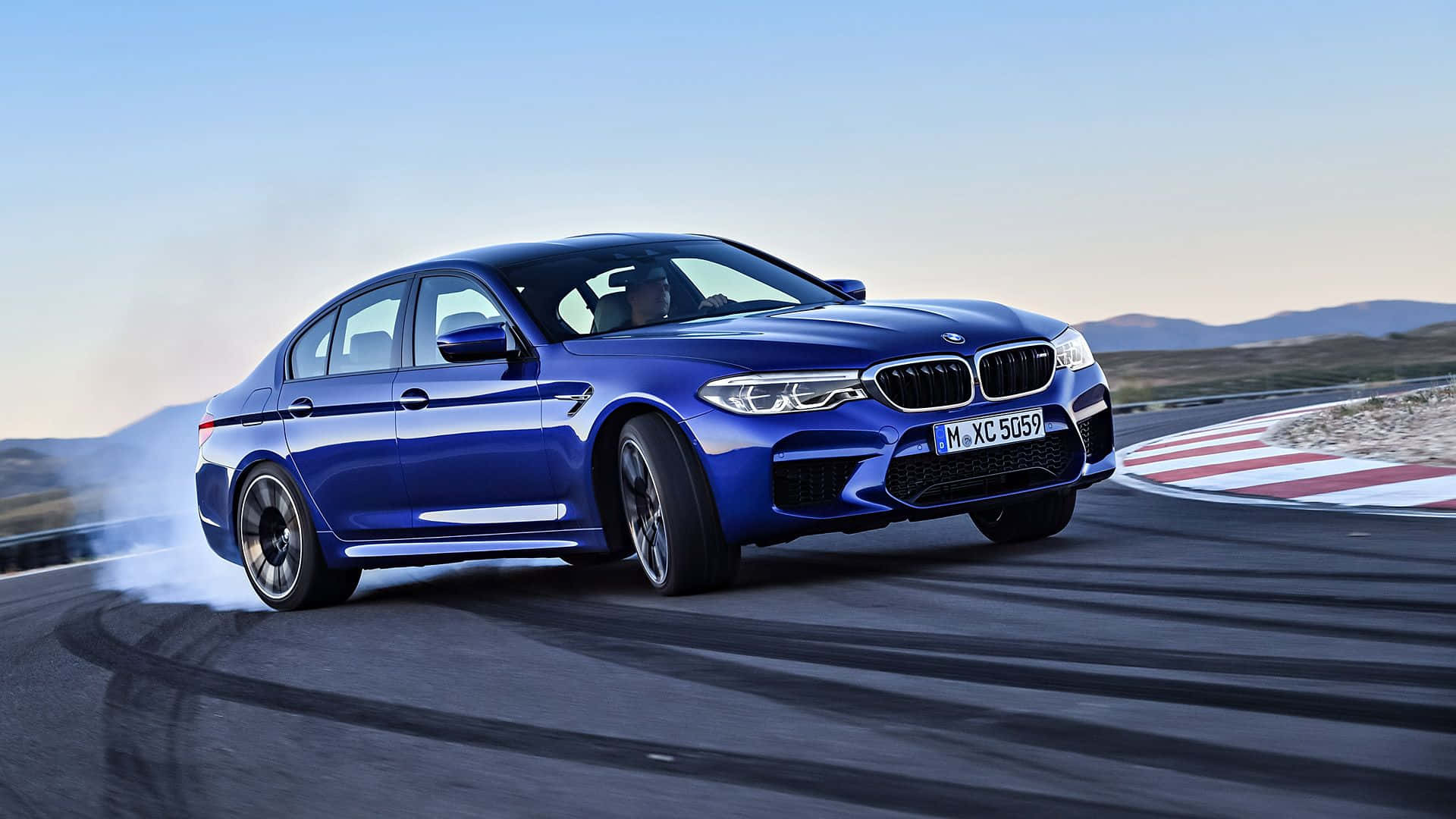 動感十足的BMW M5在公路上飛馳 壁紙 — 一輛鮮藍色寶馬M5在賽道彎位飄移，在晴朗天空下揚起煙霧。