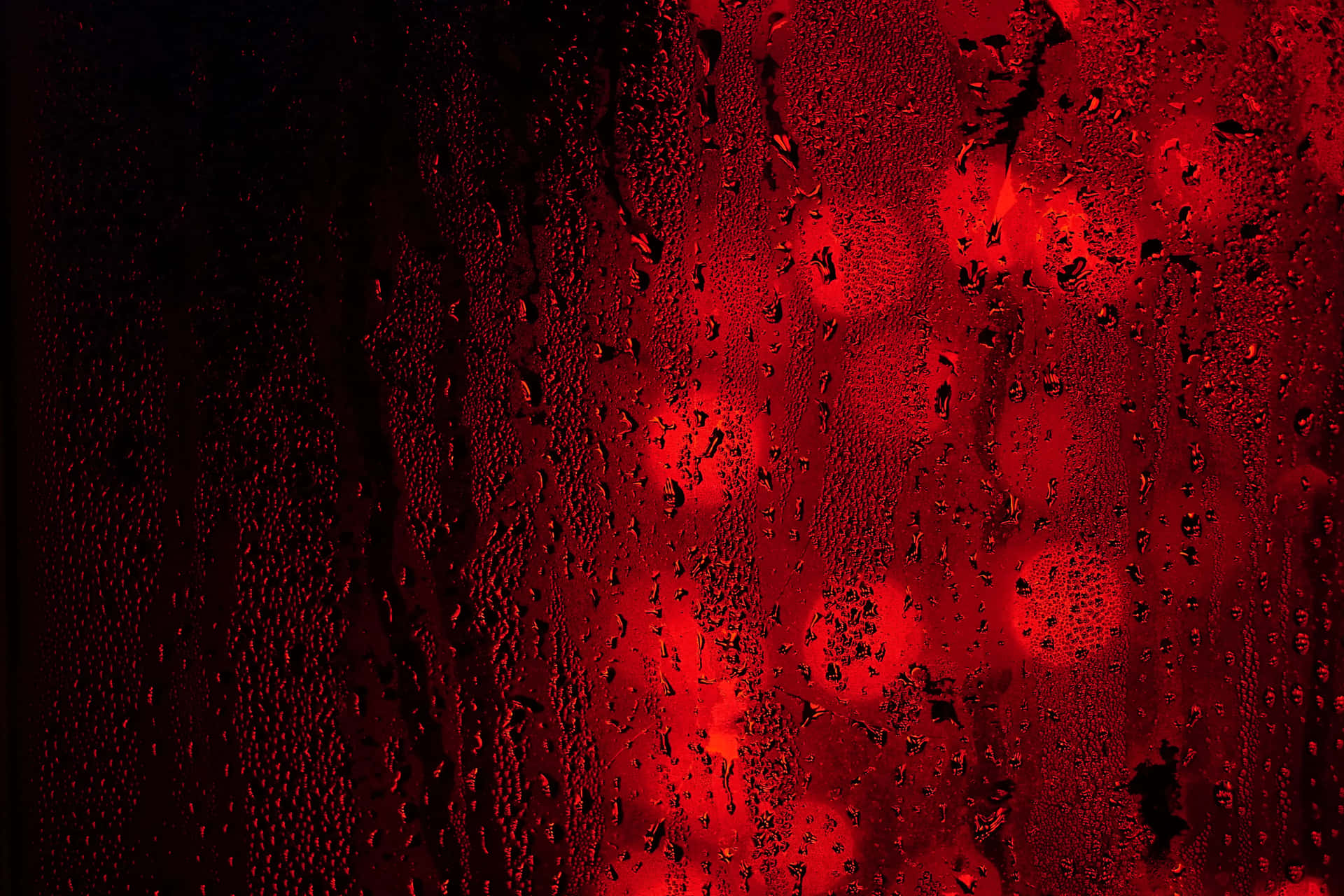 夜晚，窗戶上的雨滴和外面模糊的紅色燈光。