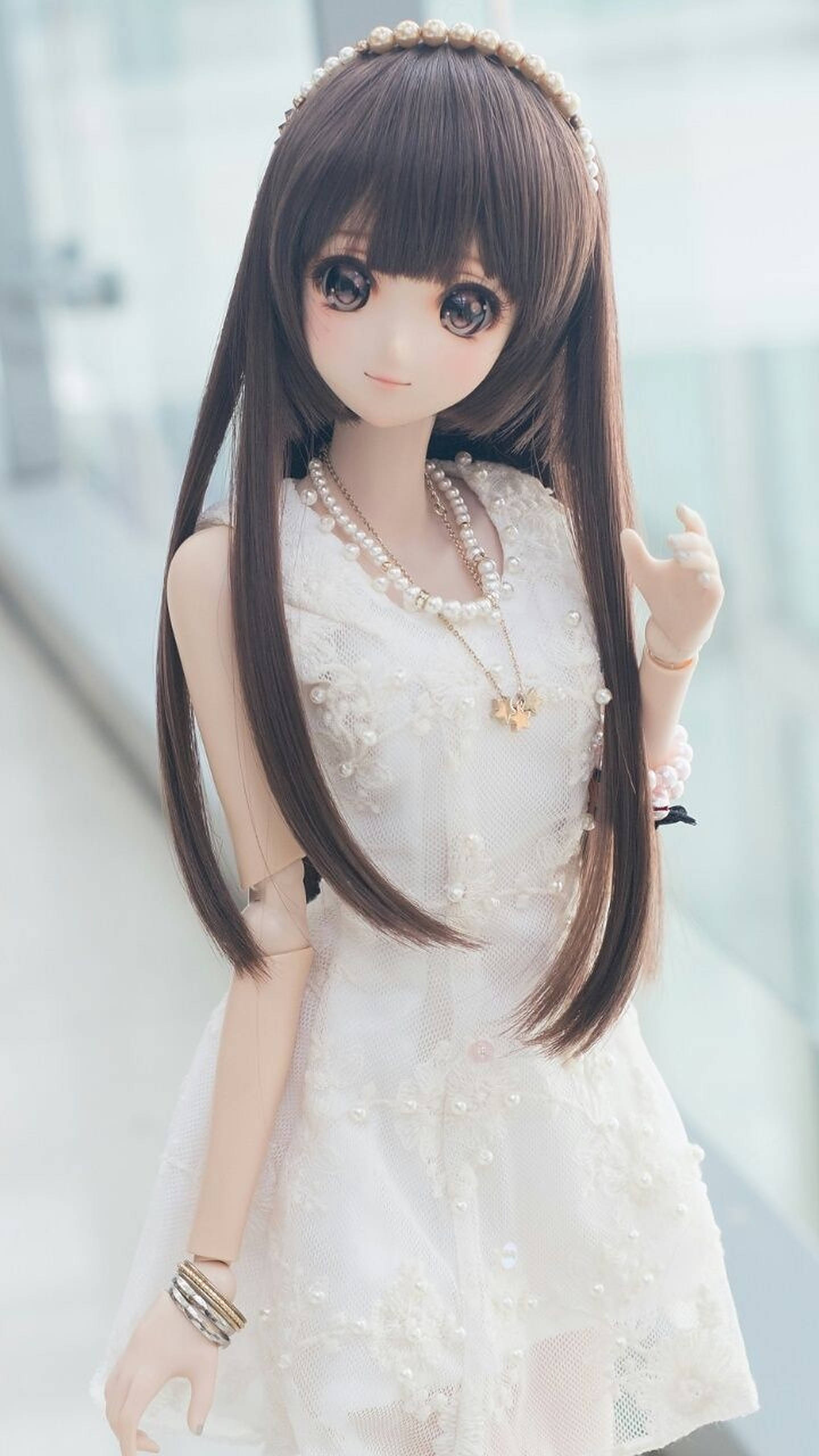 動漫少女玩偶 壁紙 — 一個擁有長長棕色頭髮和珍珠配飾的洋娃娃，穿著精緻的白色蕾絲連衣裙，背景明亮模糊。